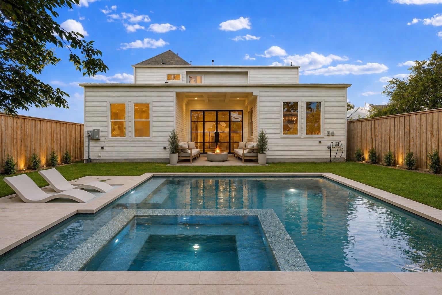 Backyard pool and raised spa in front of a white home with a covered patio.