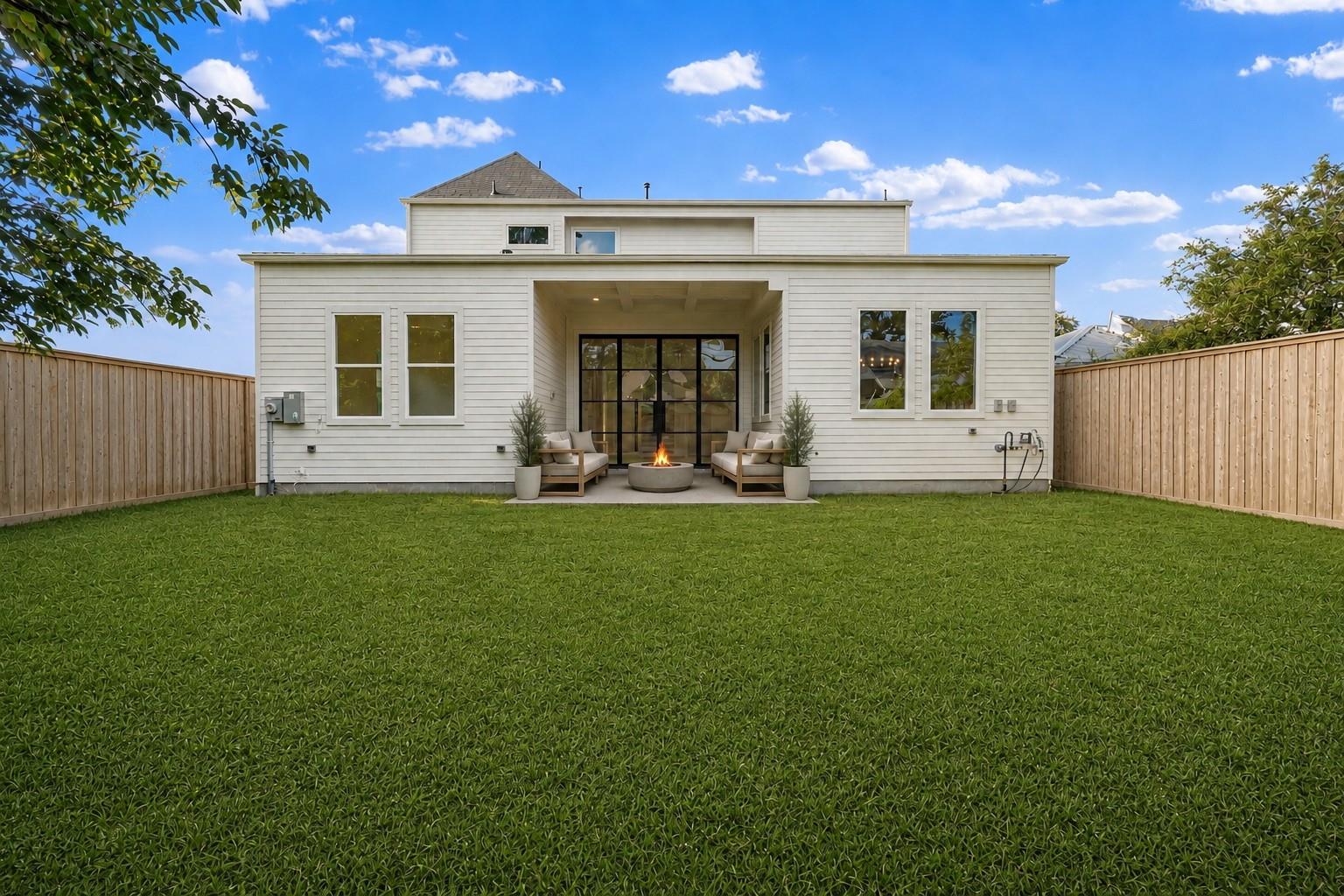 White two-story home with a covered patio, seating, fire pit, and fenced lawn.