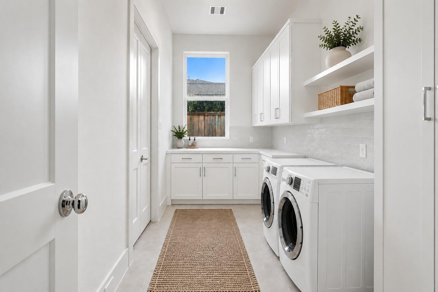 Bright laundry room with white cabinets, front-loading washer and dryer, and open shelves.