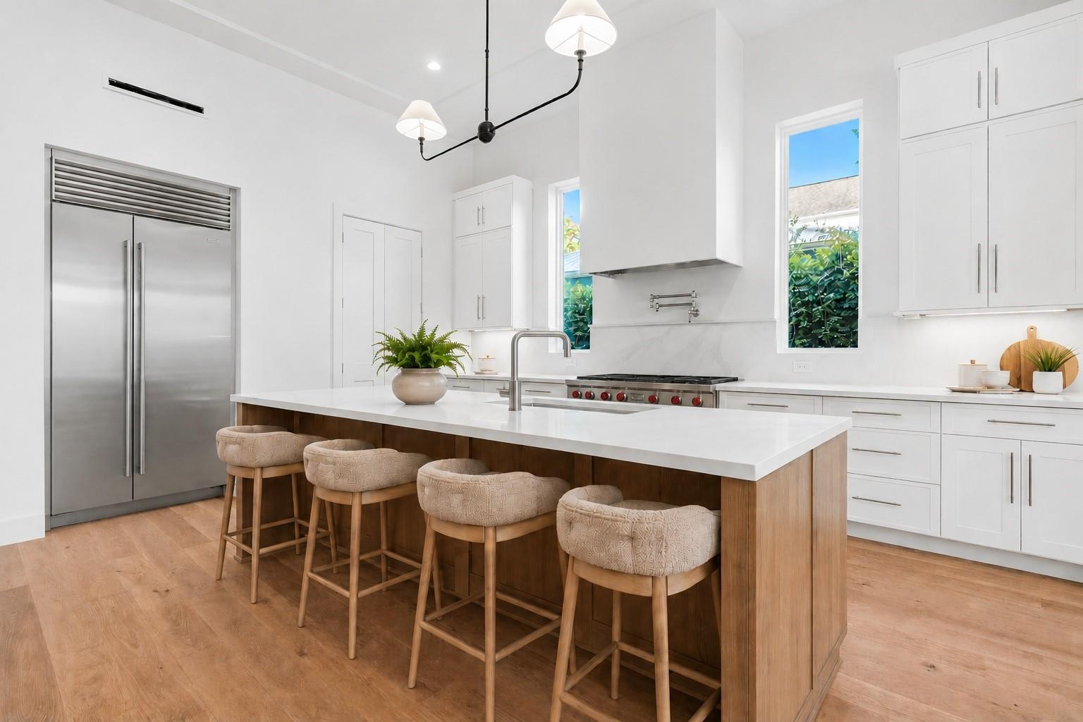 Modern white kitchen with a large wood-paneled island, four upholstered stools, and stainless steel appliances.