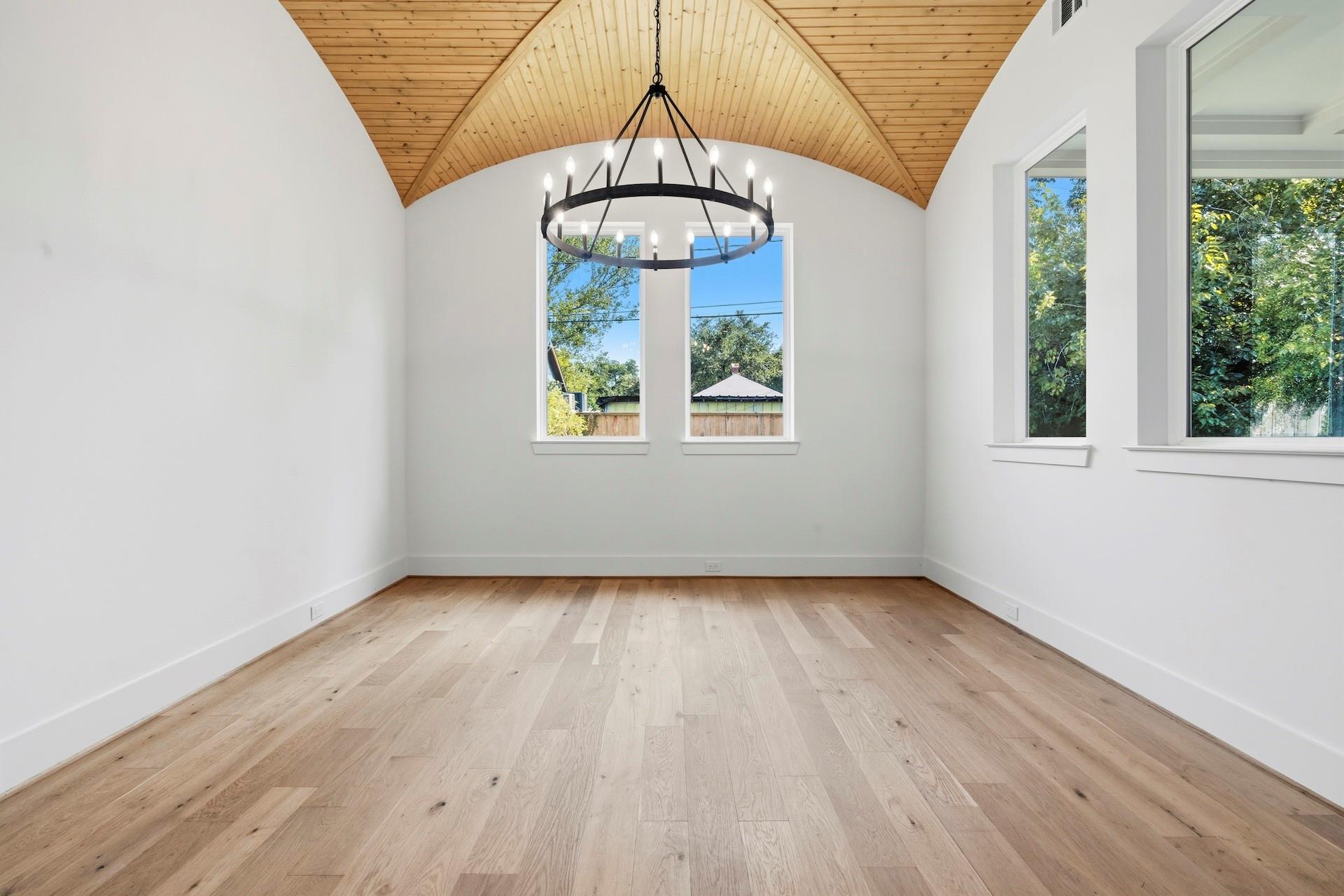 Empty room with vaulted wood ceiling, pale floors, tall windows, and a circular chandelier.