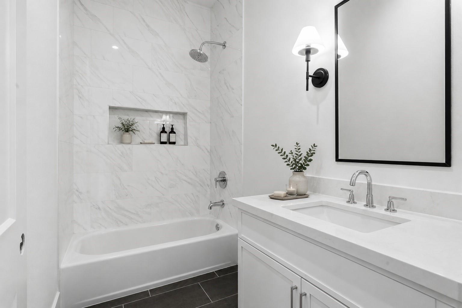 Bathroom with a white tub, marble-look shower tile, built-in niche, and white vanity.