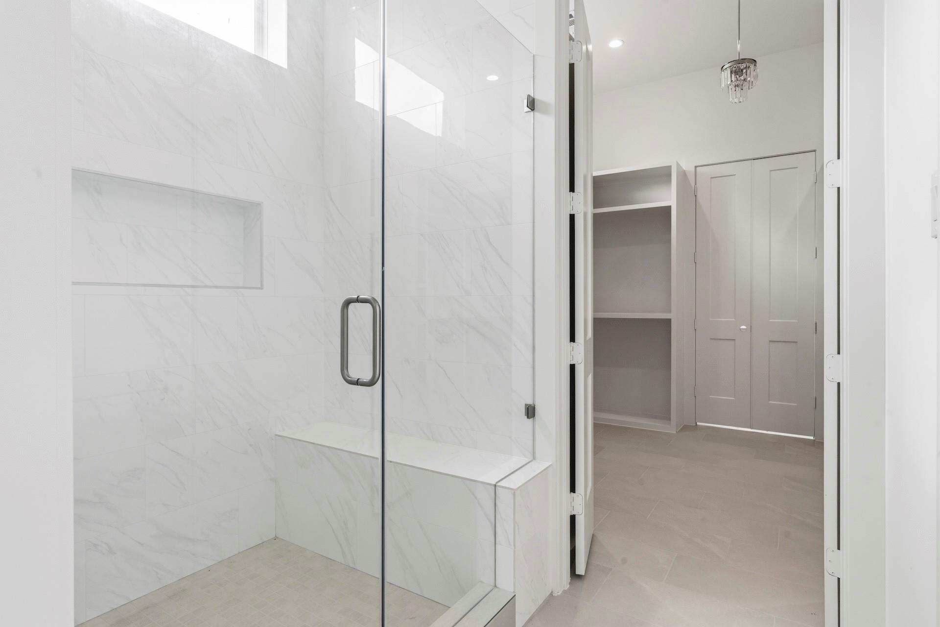 Bathroom with a marble-look walk-in shower, glass enclosure, built-in bench, and recessed niche.