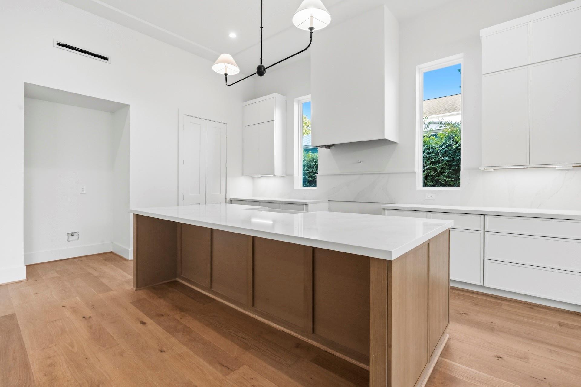 Modern kitchen with a large wood-paneled island, white cabinetry, and light wood floors.