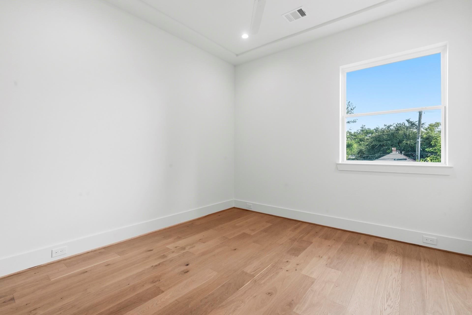 Empty room with light hardwood floors, a tray ceiling, and a large window overlooking trees.