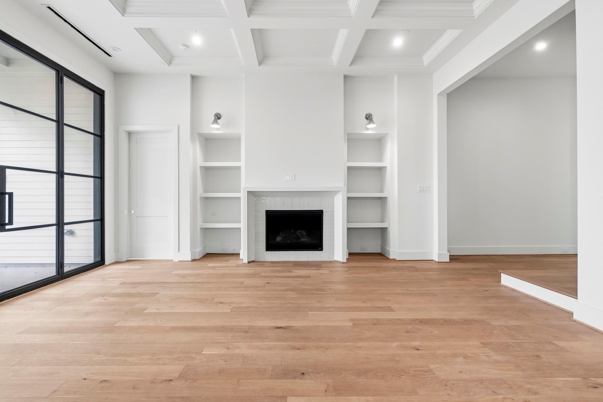 Living room with a white fireplace, built-in shelves, coffered ceiling, and black-framed sliding glass doors.