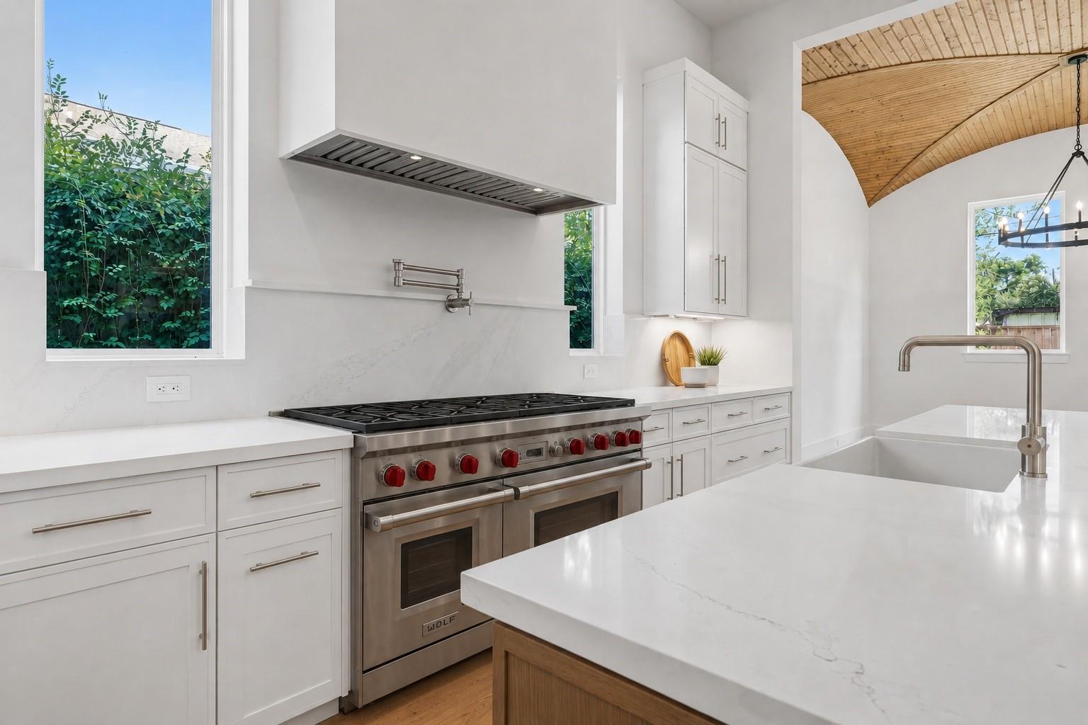 Modern white kitchen with a large stainless range, quartz island, and vaulted wood-plank ceiling.