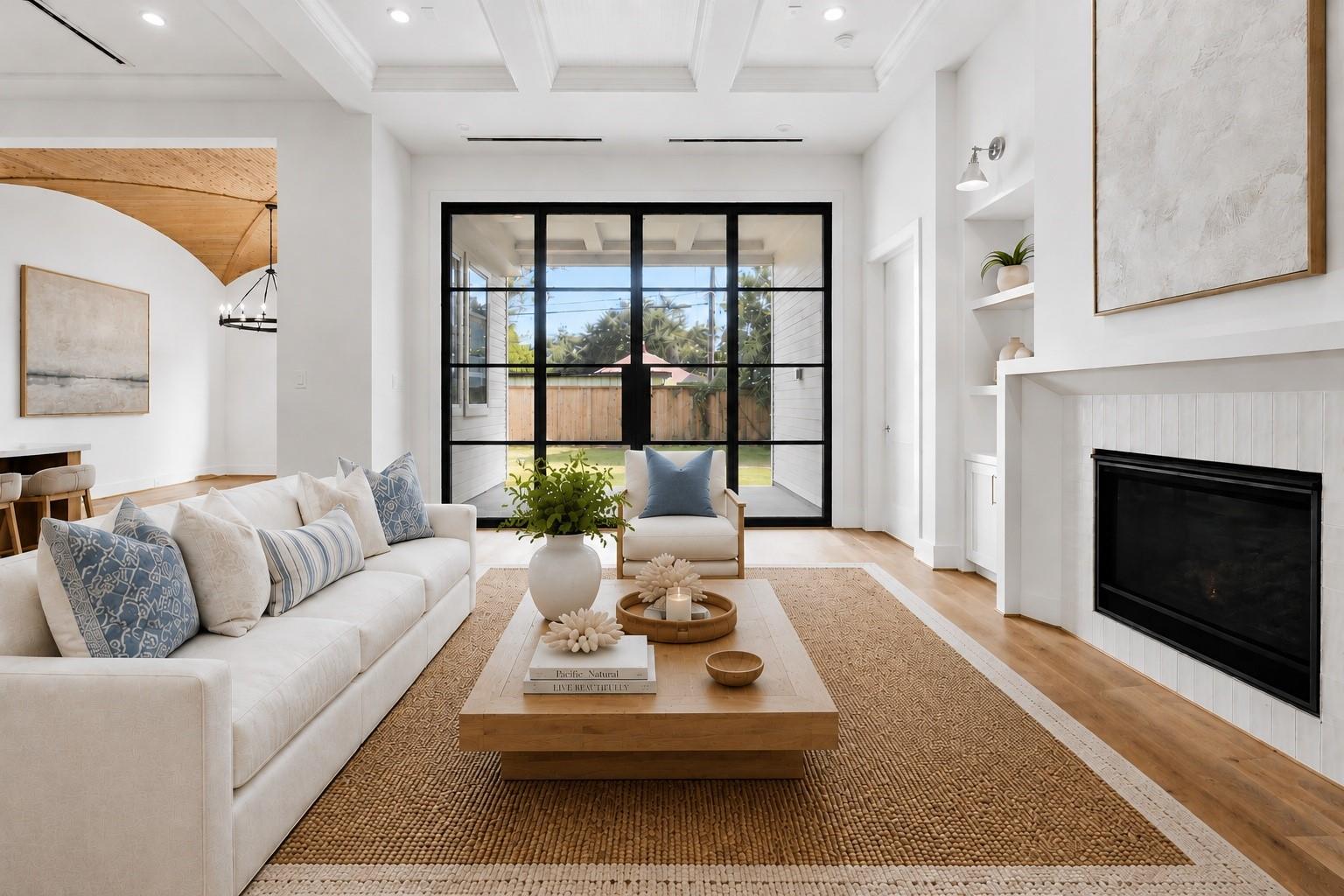 Living room with a modern fireplace, coffered ceiling, and black-framed doors to the backyard.