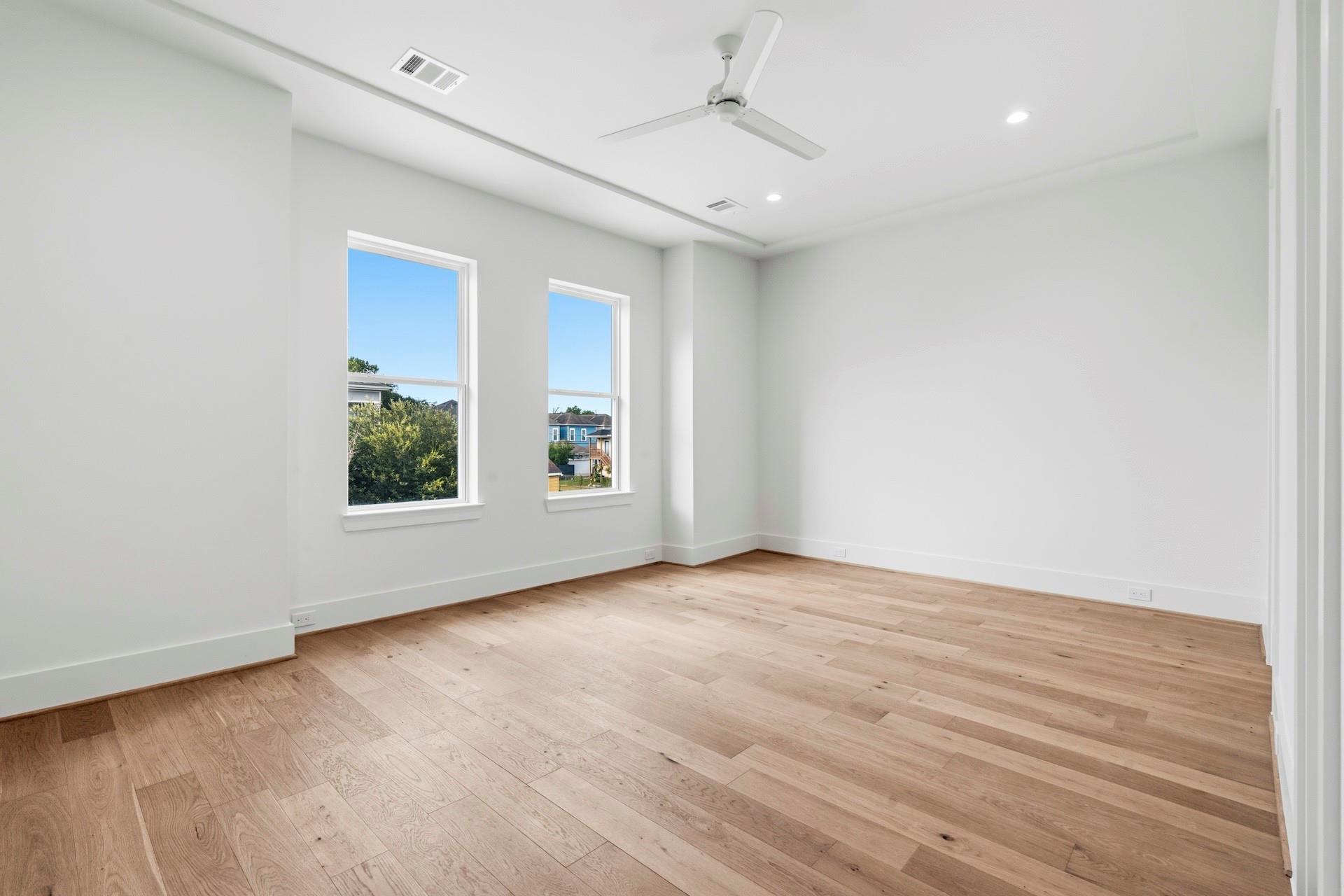 Empty room with light wood floors, two windows, and a modern ceiling fan.