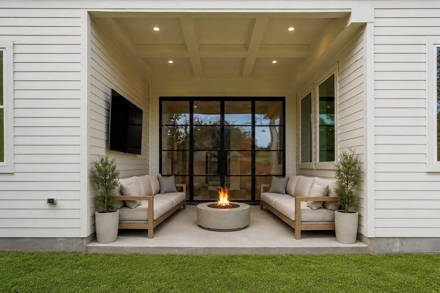 Covered patio with matching sofas and a round fire pit in front of black-framed glass doors.