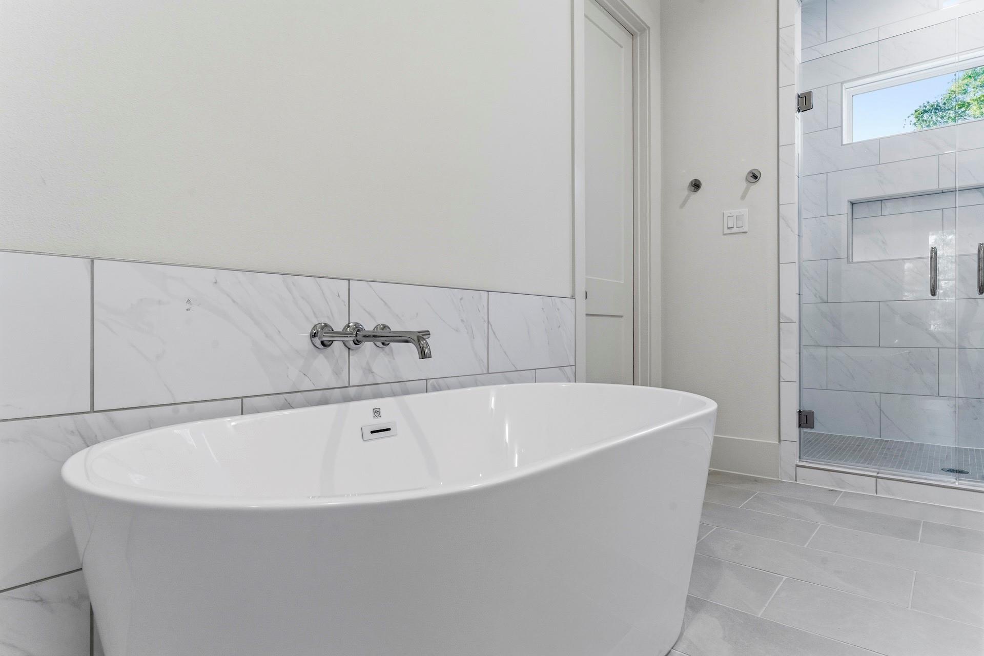 Bathroom with freestanding soaking tub and glass-enclosed shower lined in marble-look tile.
