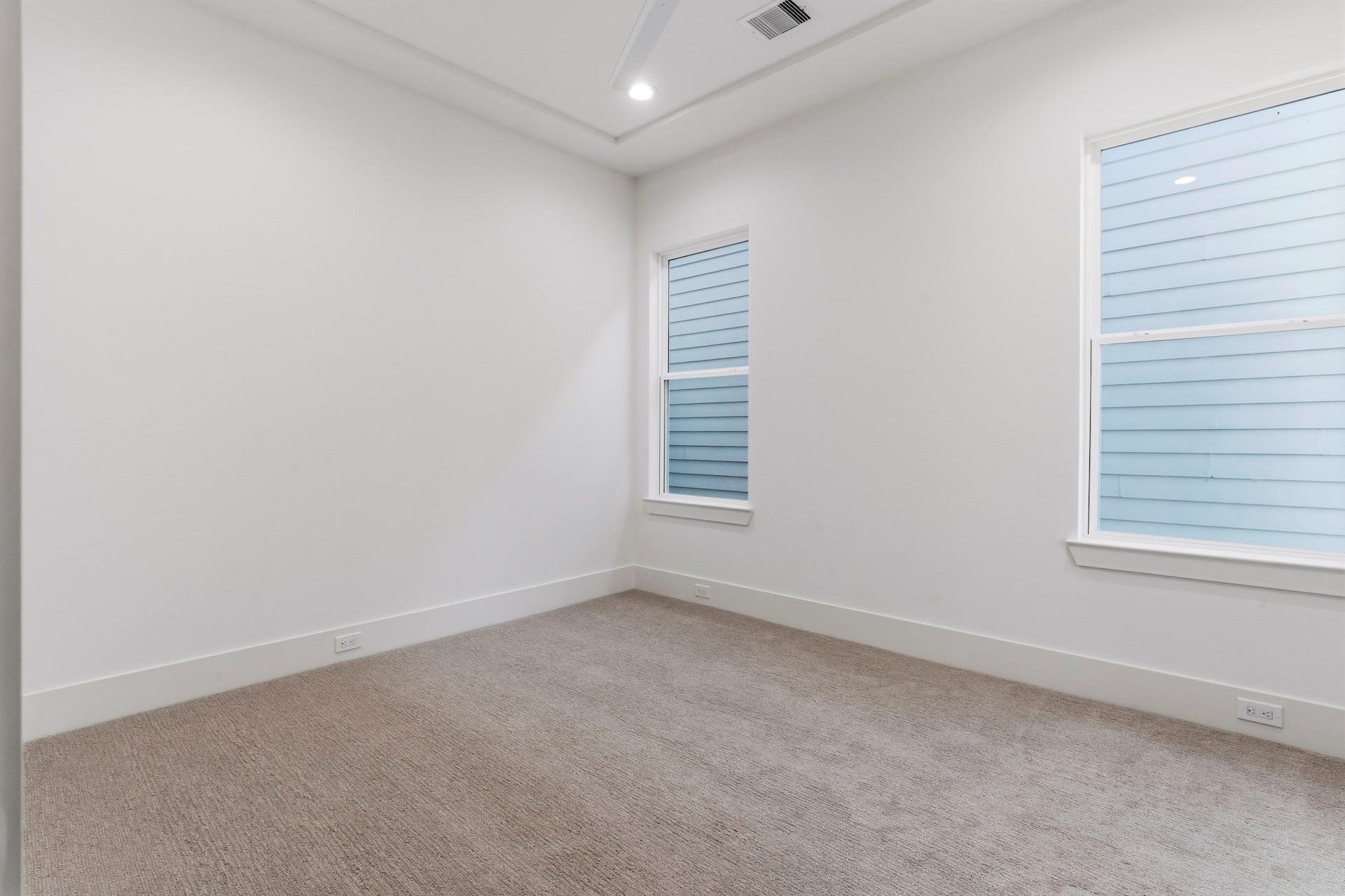 Empty carpeted room with white walls, two windows, and a recessed ceiling.