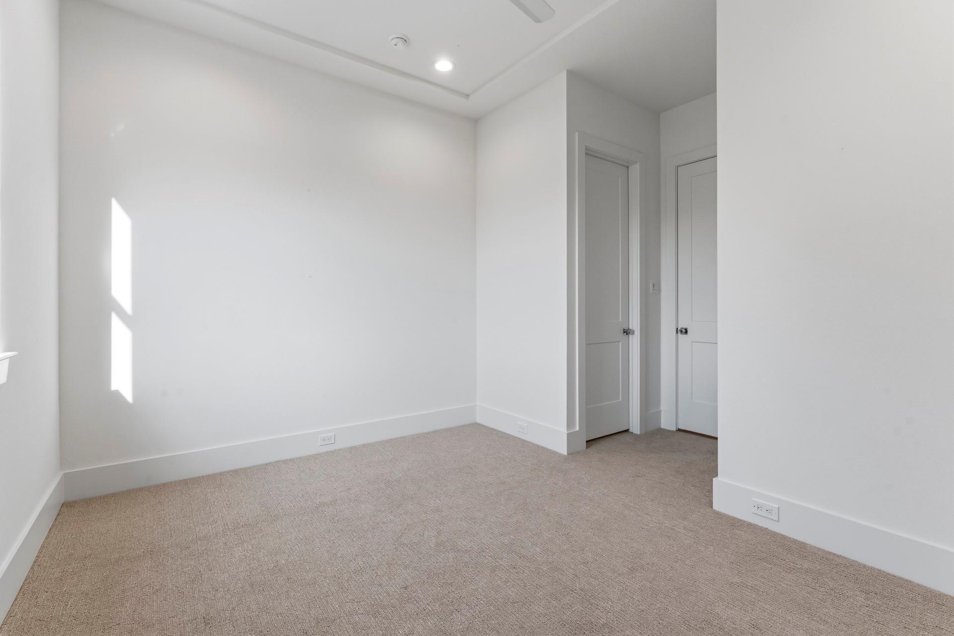 Empty bedroom with beige carpet, a tray ceiling, and two paneled doors.