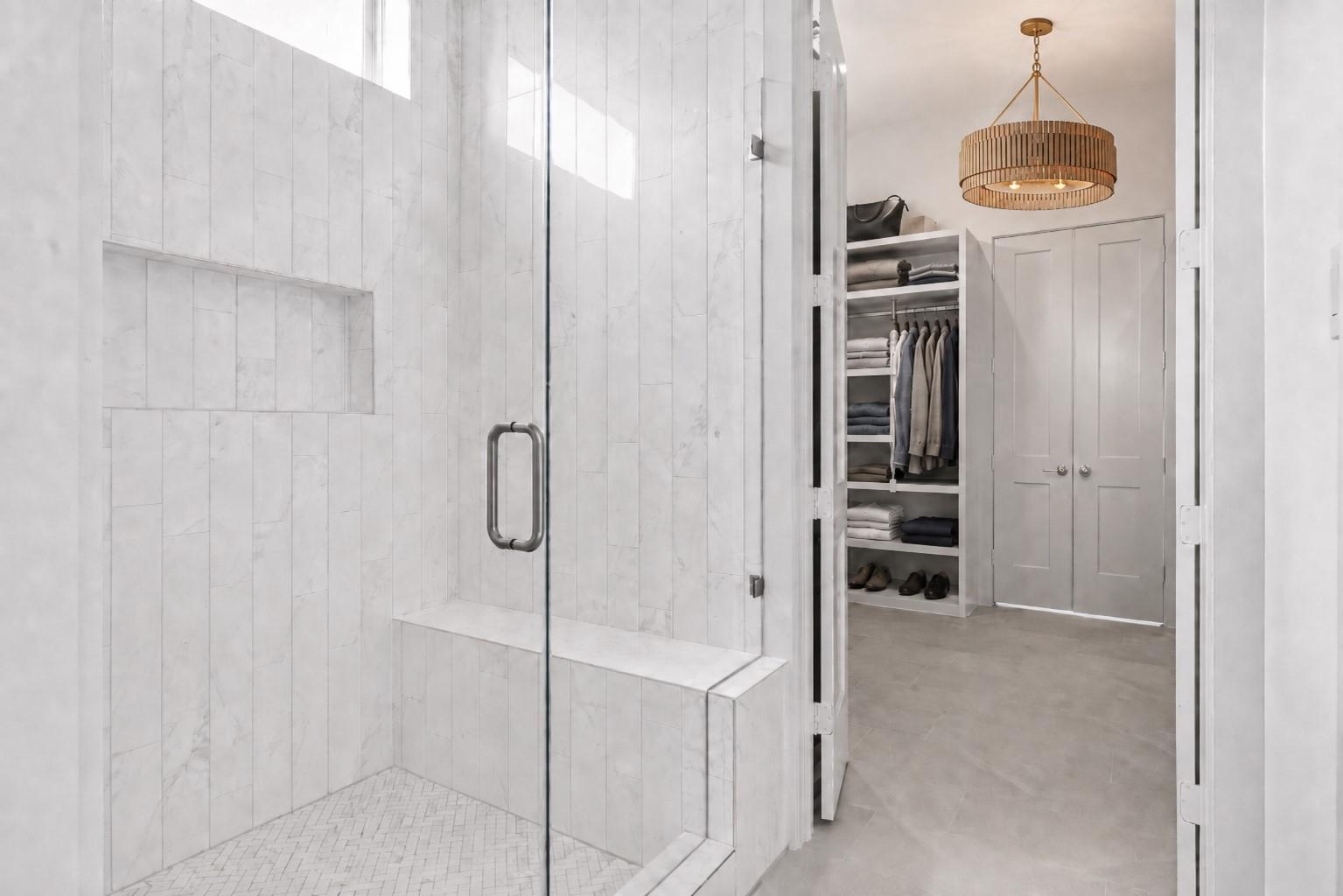 Marble-tiled shower with glass enclosure and bench beside an organized walk-in closet.