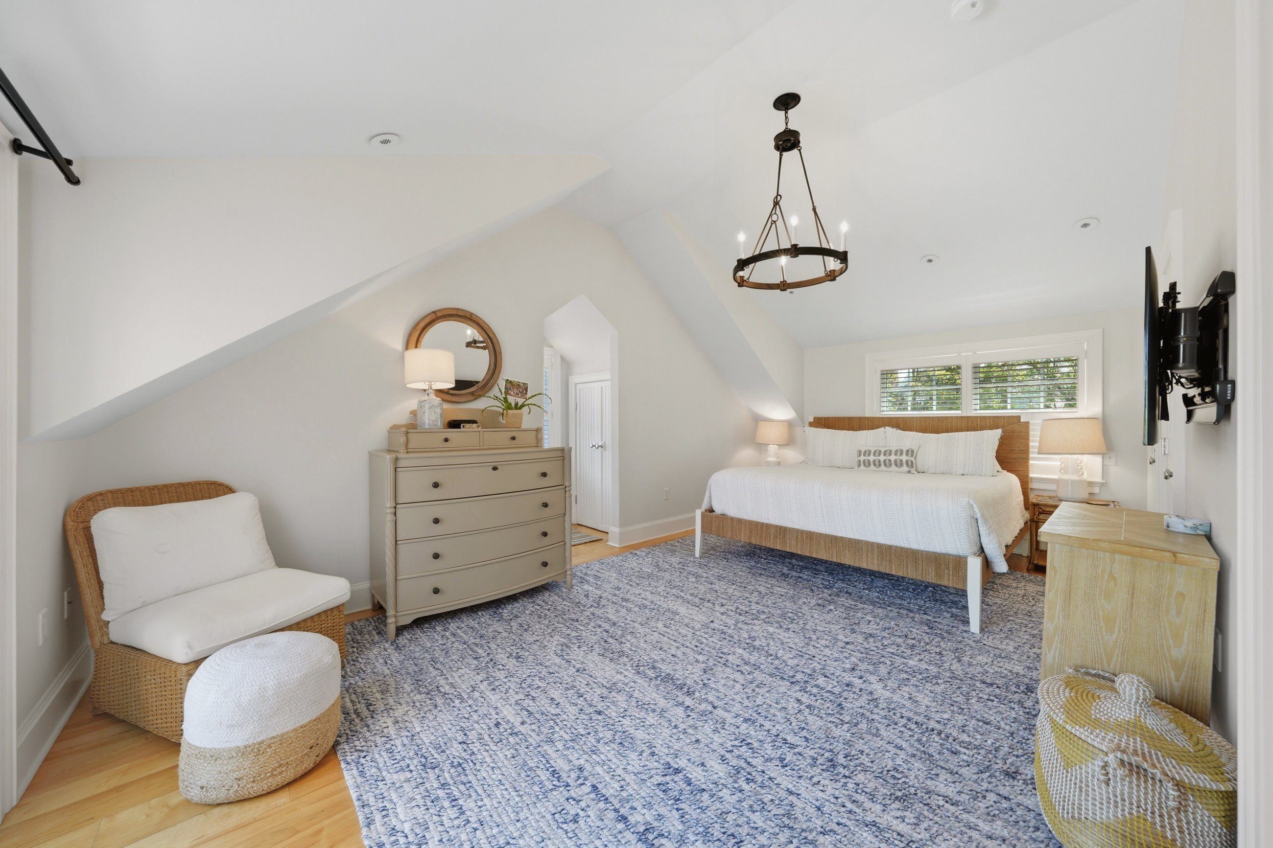 Furnished bedroom with a white bed, shuttered windows, sloped ceiling, and blue patterned rug.