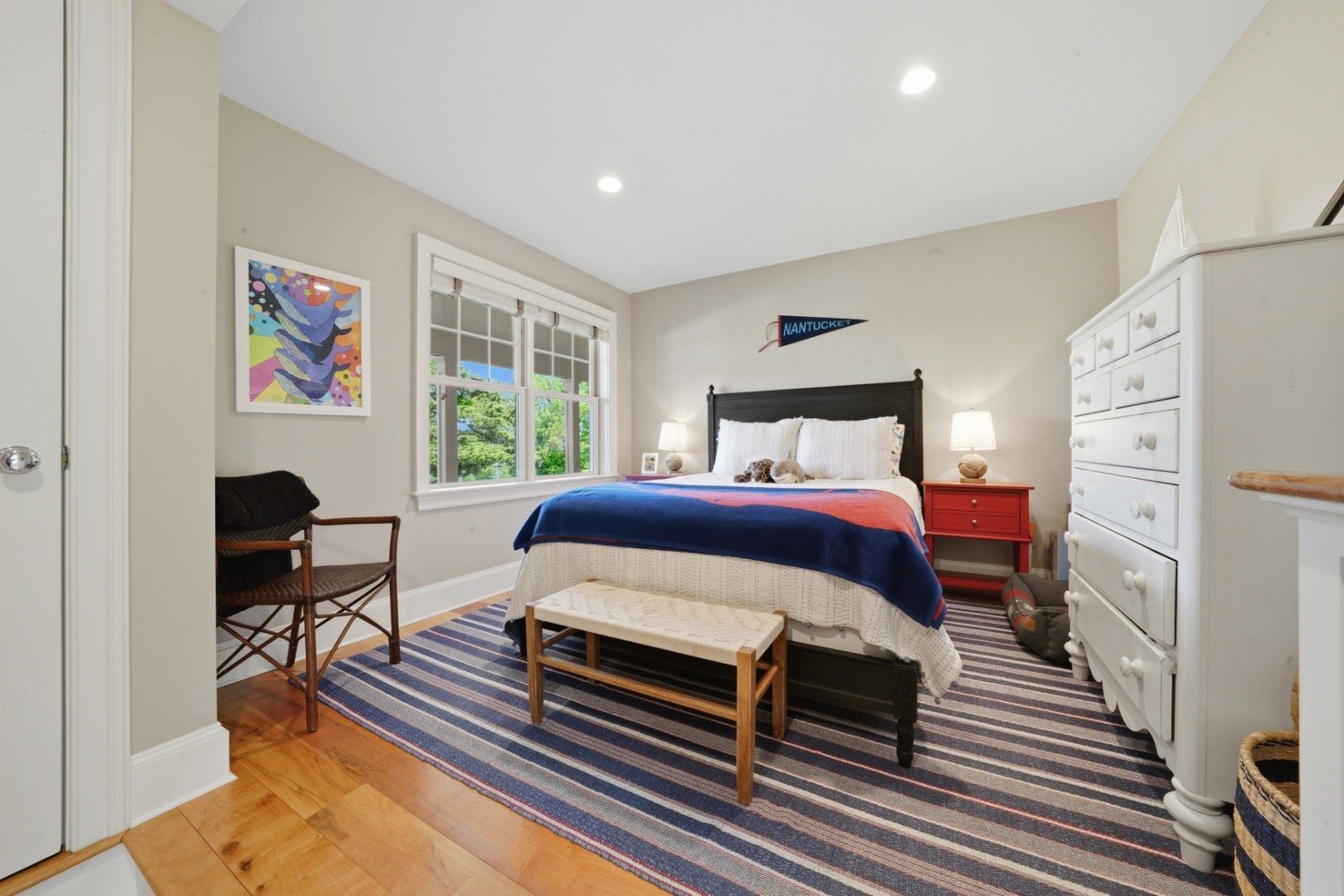 Bedroom with a navy-and-red bedspread, striped rug, and Nantucket pennant above the bed.