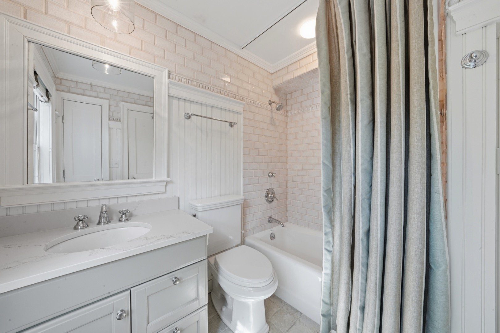Bathroom with a white vanity, toilet, and tub behind a striped shower curtain.