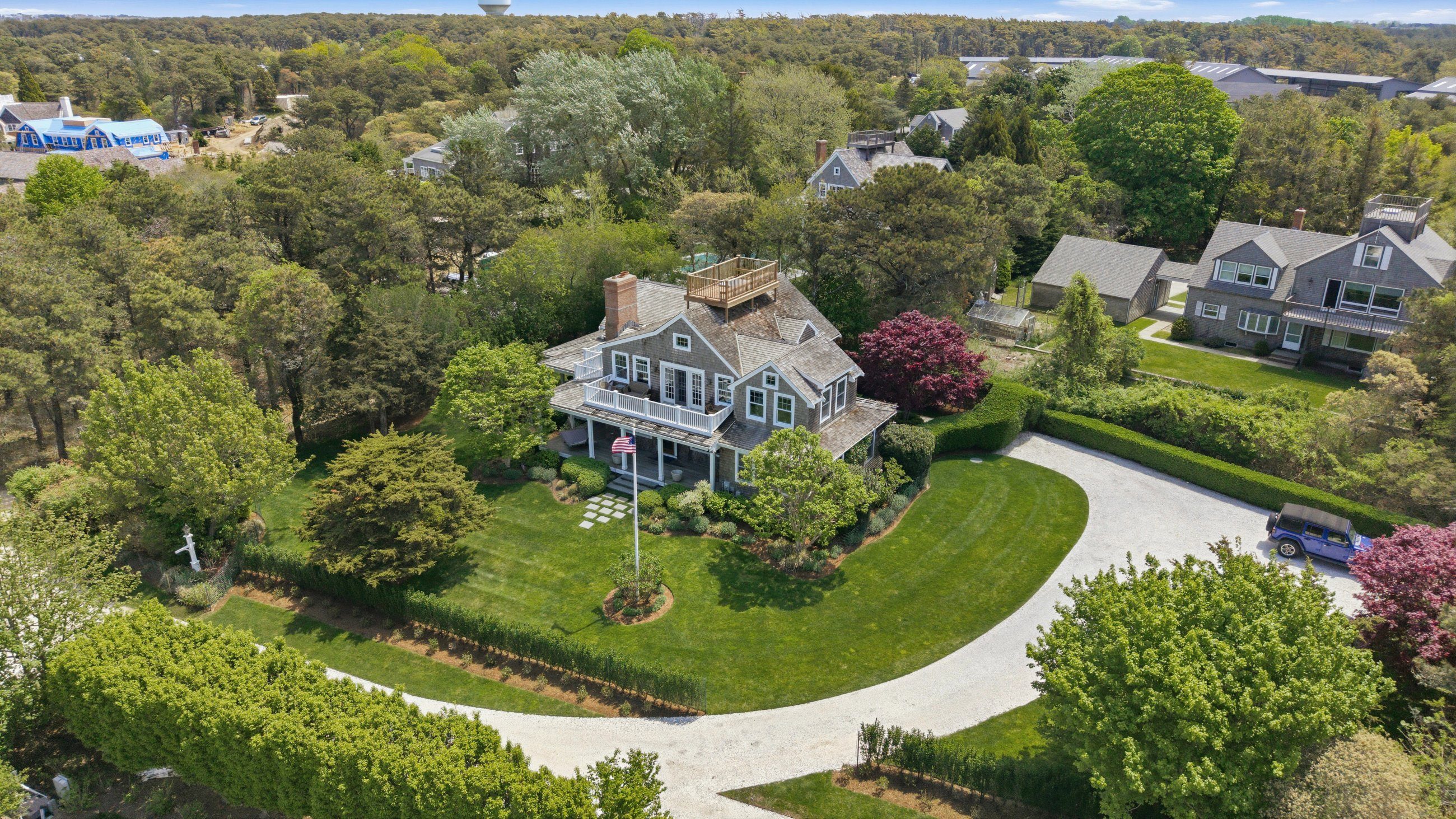 Aerial view of a gray-shingled home with a rooftop deck and curved gravel driveway.
