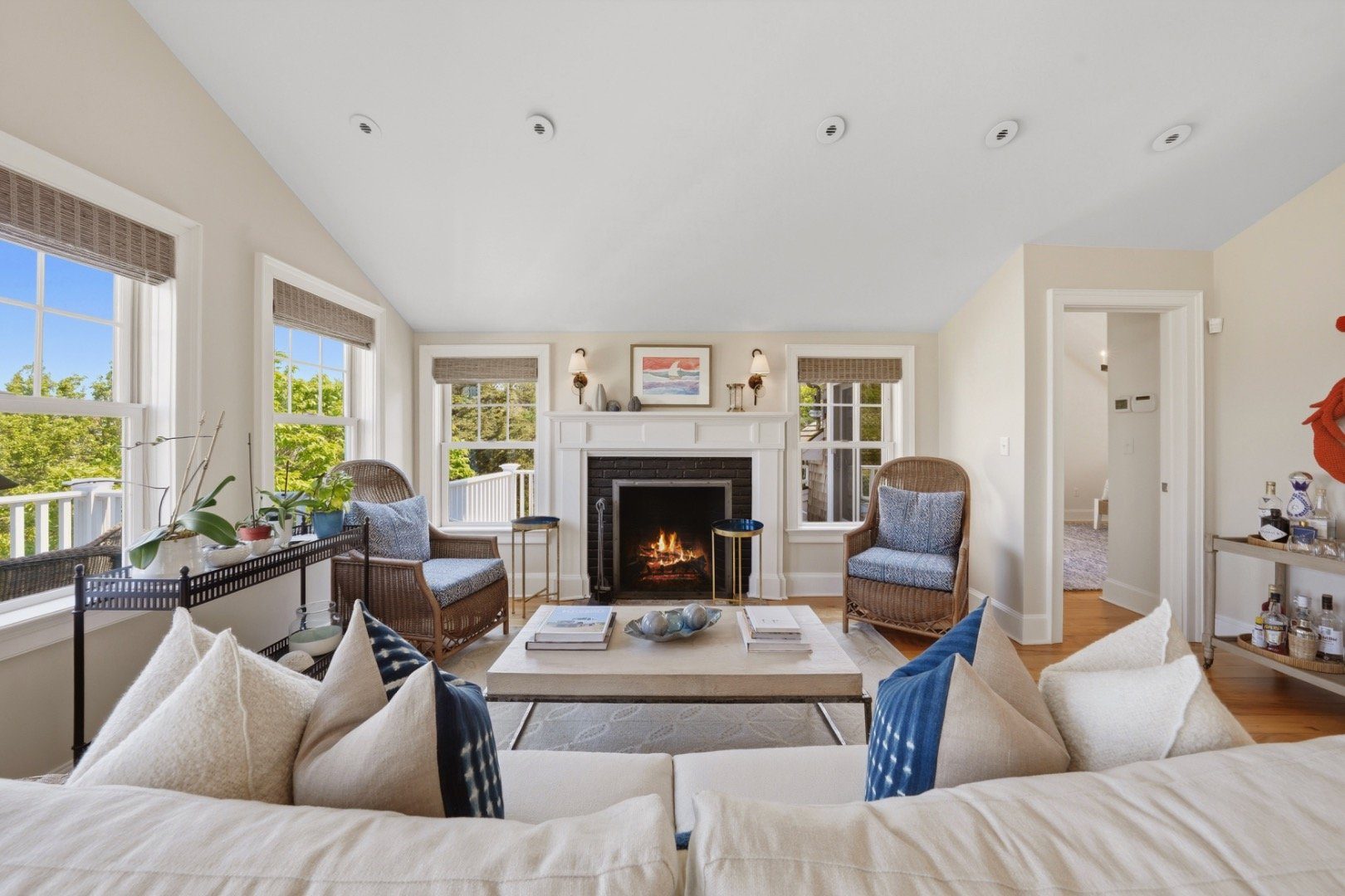 Living room with a fireplace, vaulted ceiling, white sofas, and large windows overlooking trees.