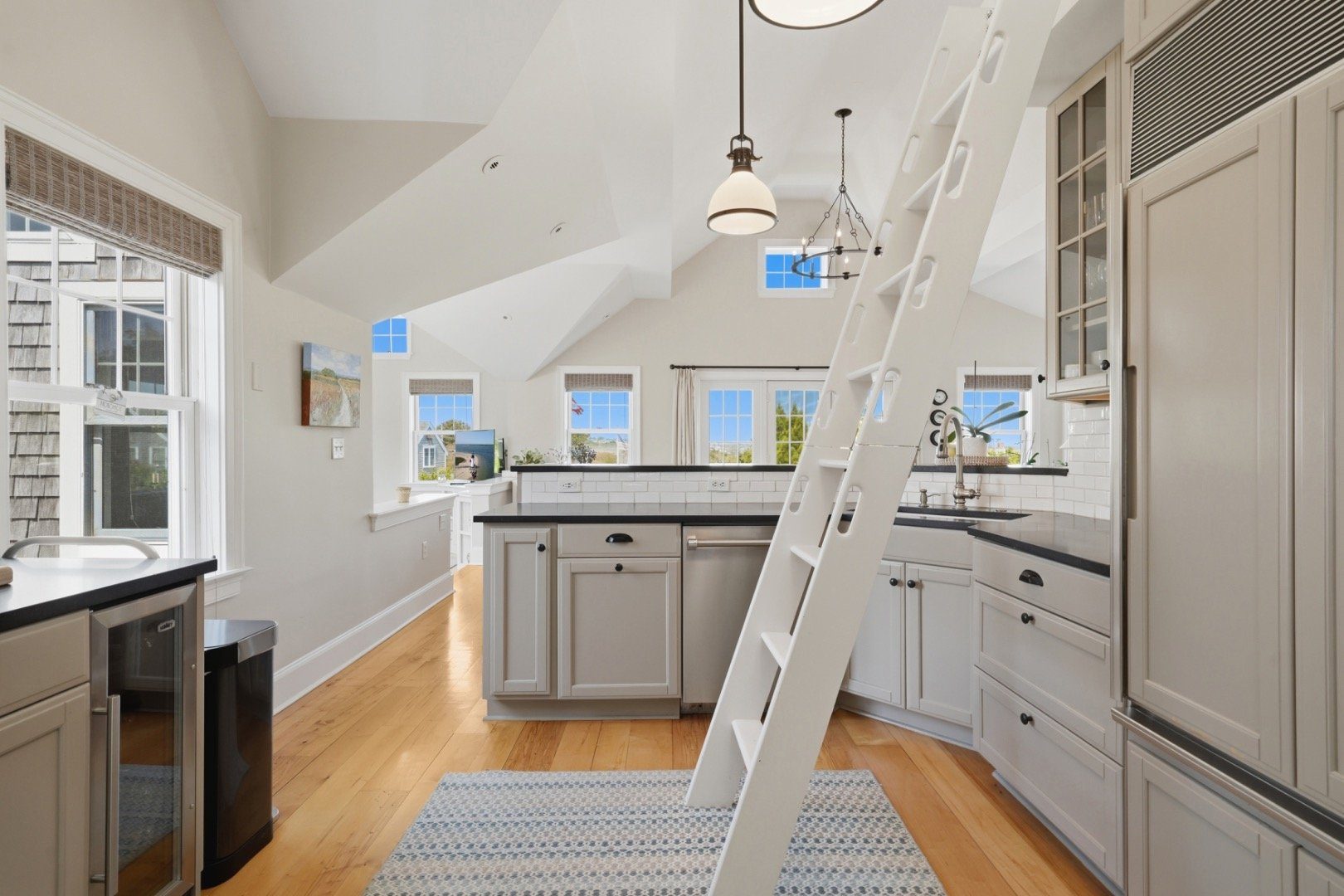 Bright white kitchen with black countertops and a ladder to the loft beneath a vaulted ceiling.