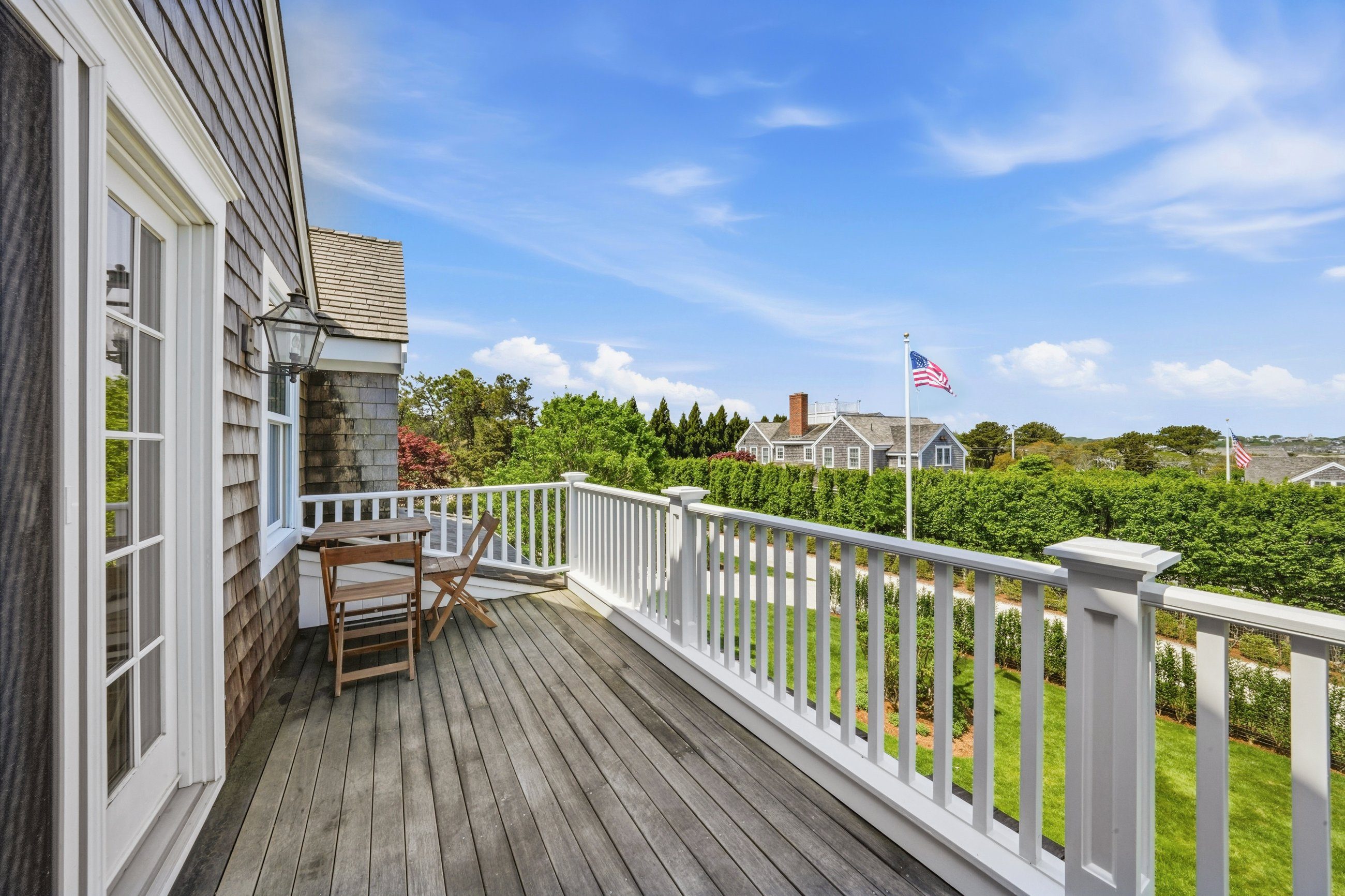 Wood deck with white railings and folding chairs overlooks hedges and neighboring homes.