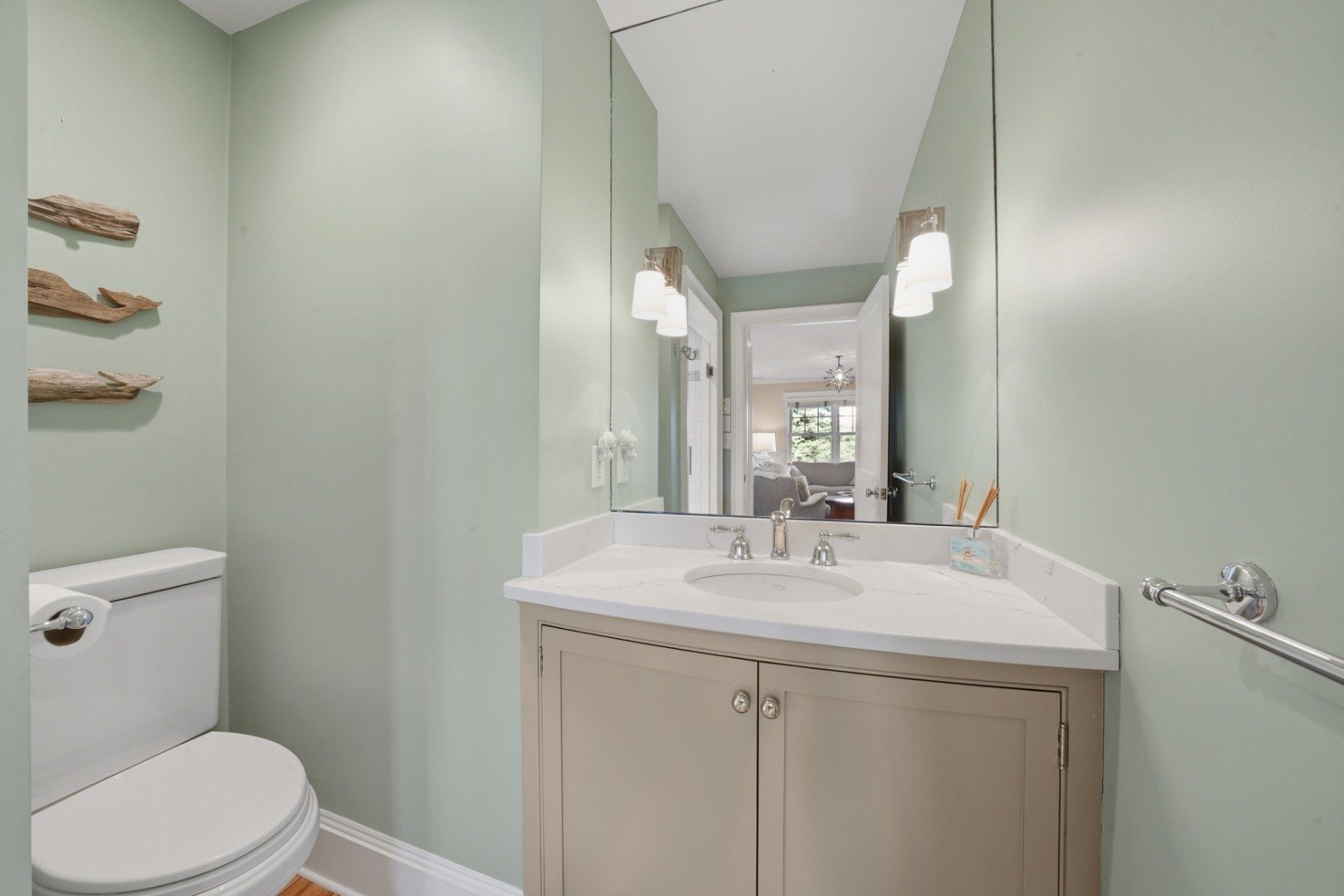 Bathroom with pale green walls, a large mirror, white sink, taupe vanity, and driftwood wall decor.