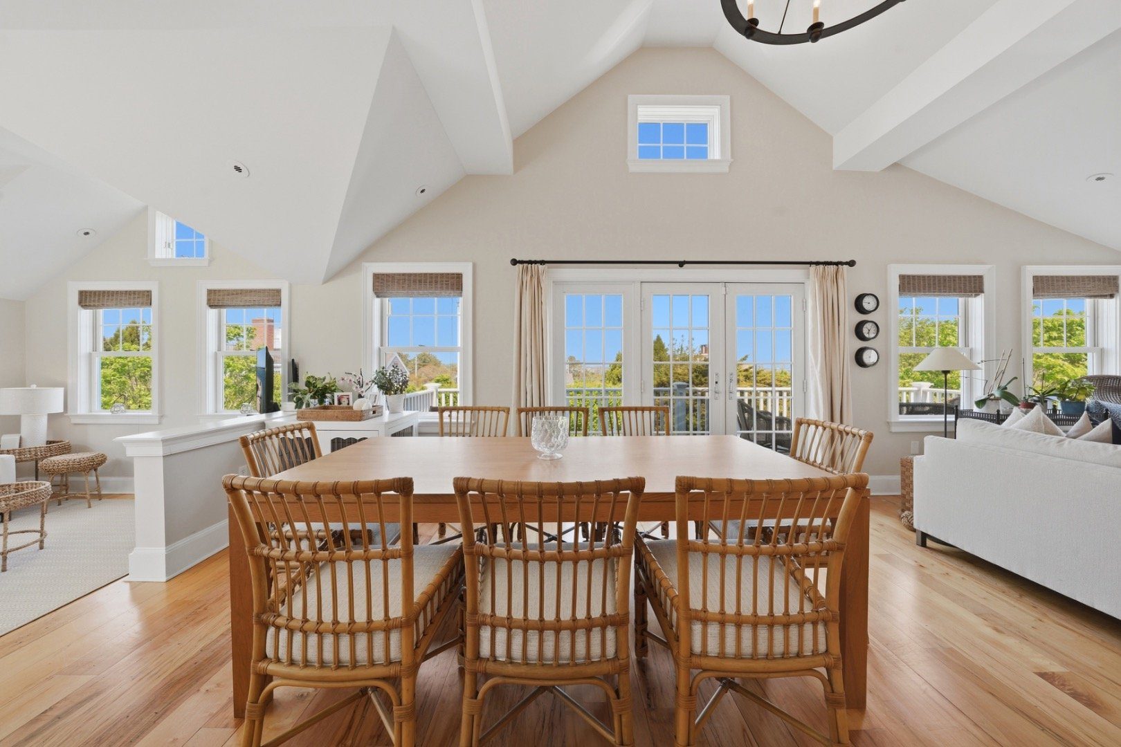 Dining area with a large wooden table, woven chairs, vaulted ceiling, and bright French doors.