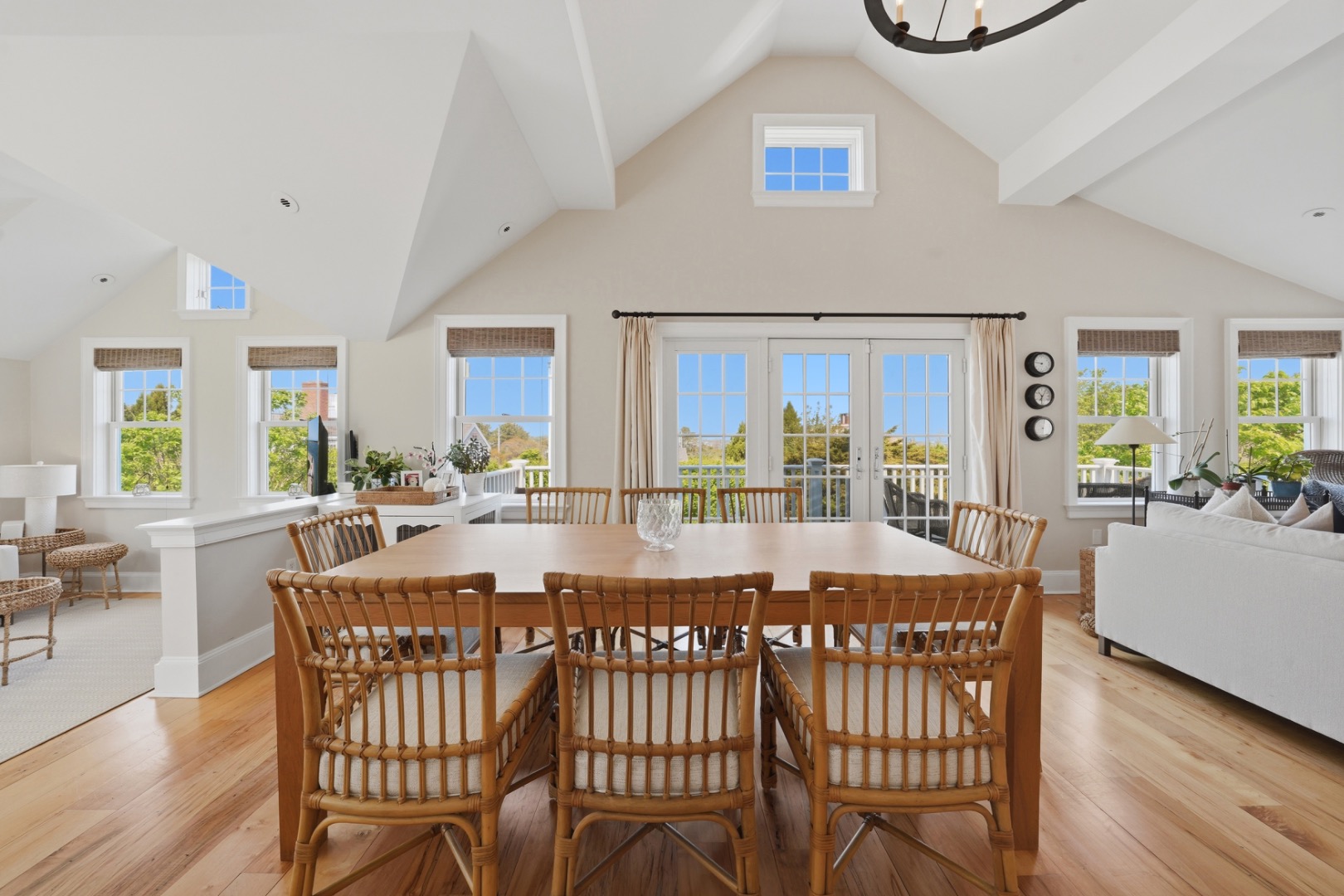 Dining room with a long wooden table, woven chairs, vaulted ceiling, and French doors.