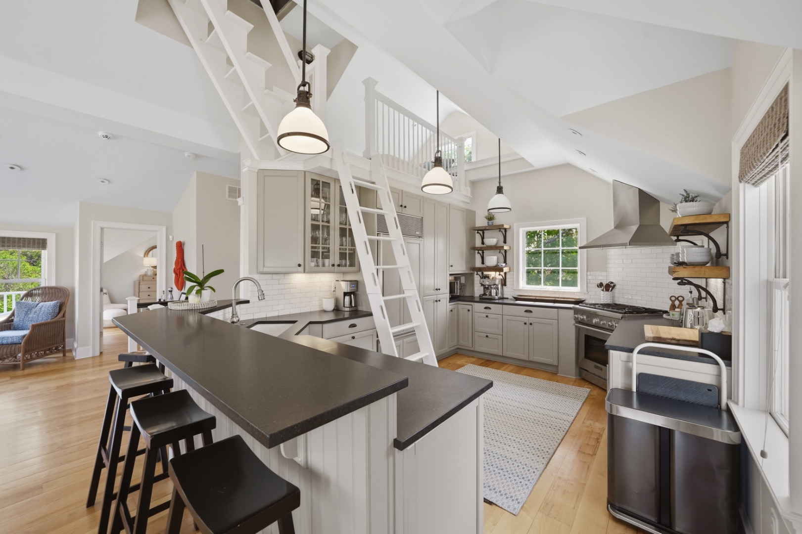 Kitchen with vaulted ceiling, dark island, white cabinetry, and a ladder to an upper loft.