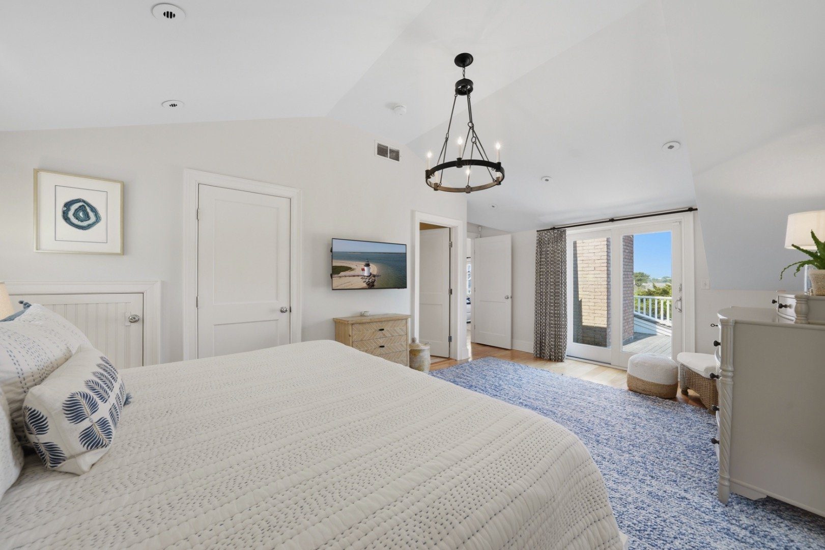 Bedroom with a white quilted bed, blue rug, and balcony doors overlooking water.