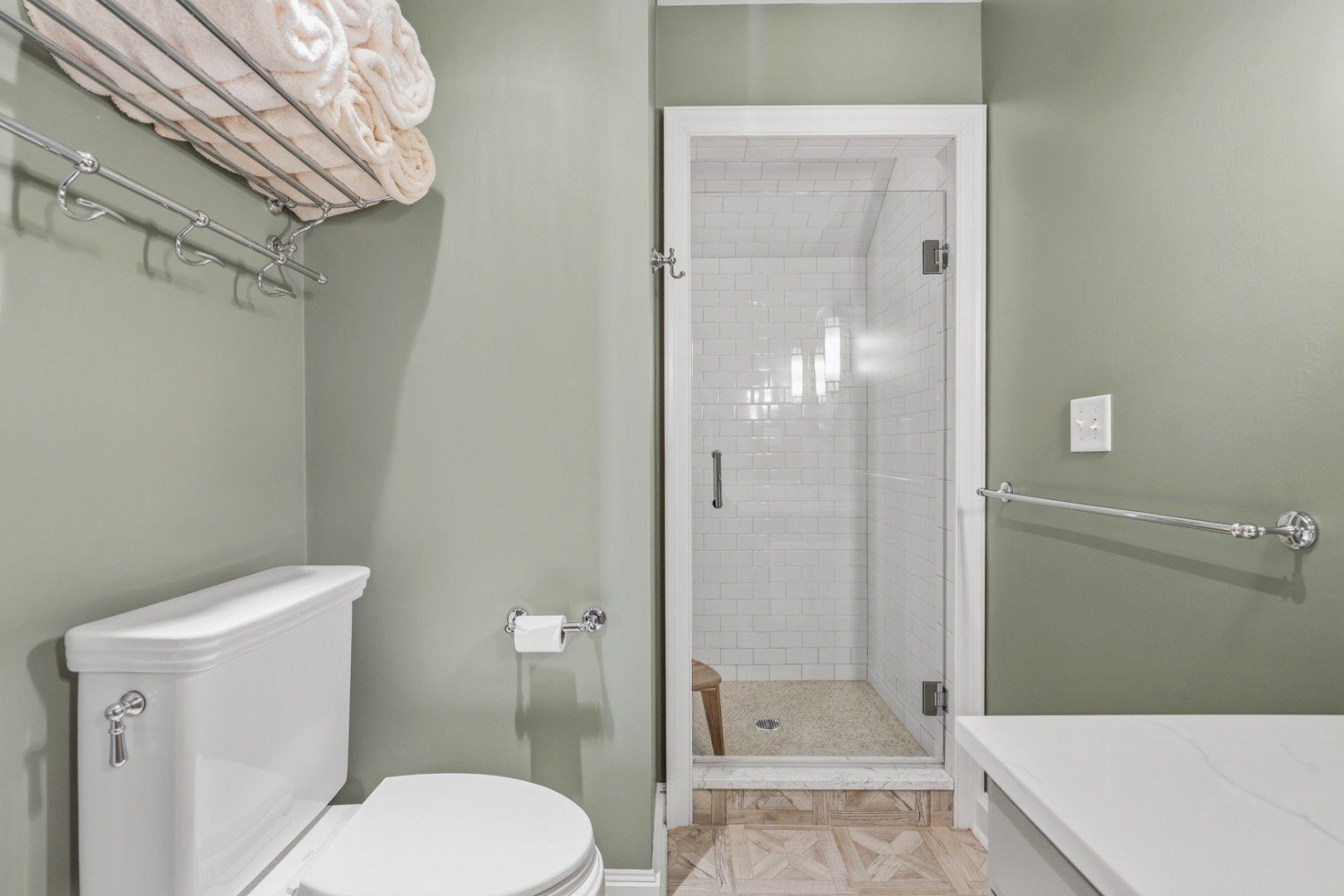 Bathroom with a glass-enclosed white subway-tile shower, pale green walls, and a white toilet.