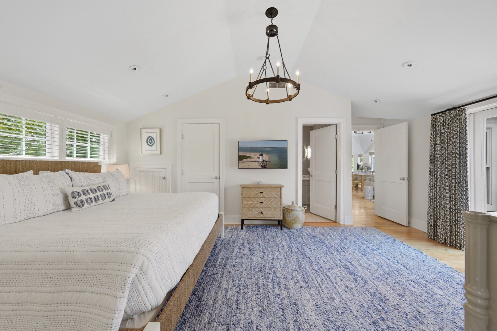 Furnished bedroom with a white quilted bed, blue rug, vaulted ceiling, and circular chandelier.