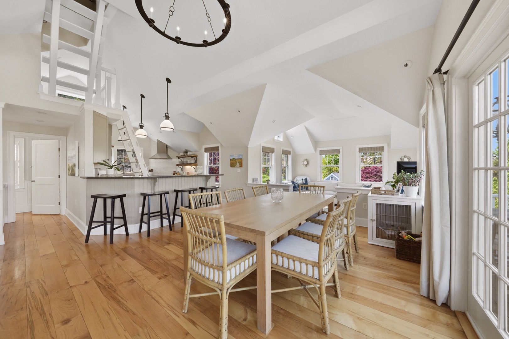 Open-plan dining room and kitchen with vaulted ceilings, a long table, and large windows.