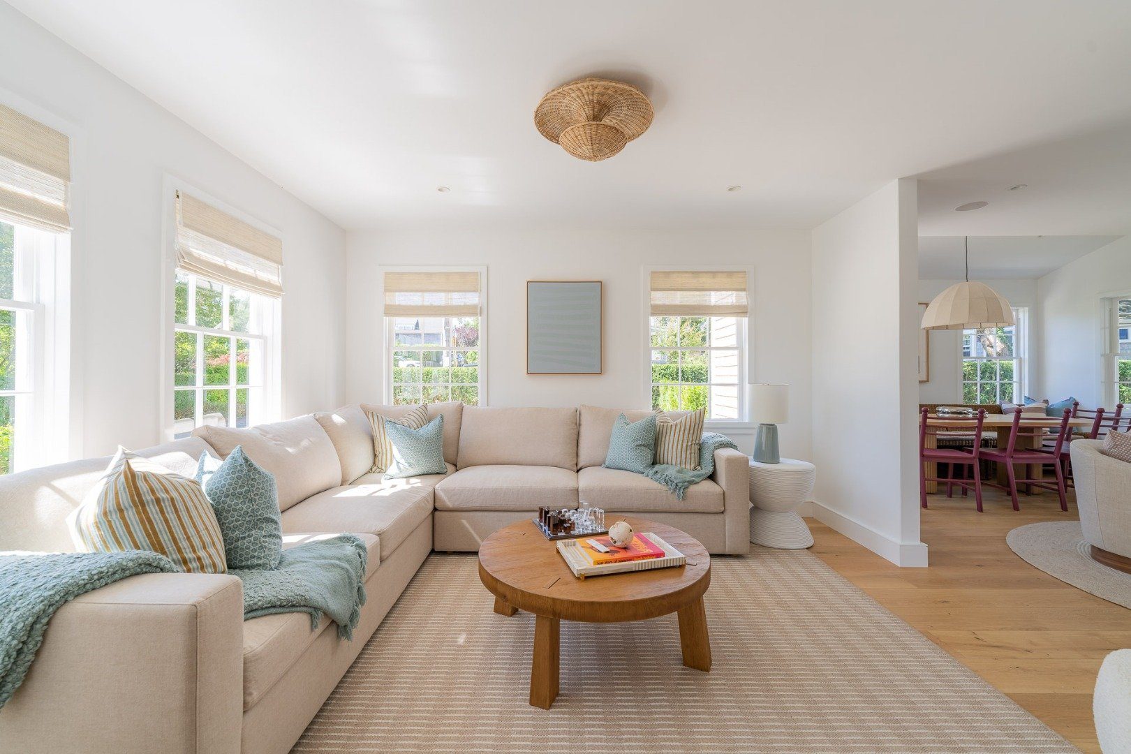 Bright living room with a cream sectional, woven ceiling light, and adjoining dining area.