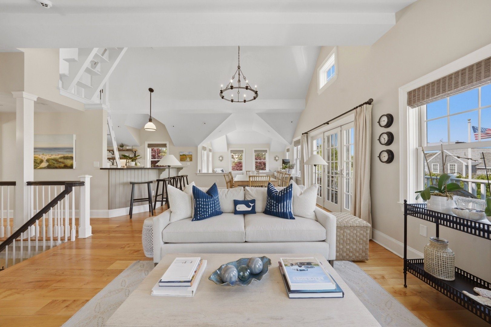 Open-plan living room with vaulted ceiling, white sofa, wood floors, and large windows.