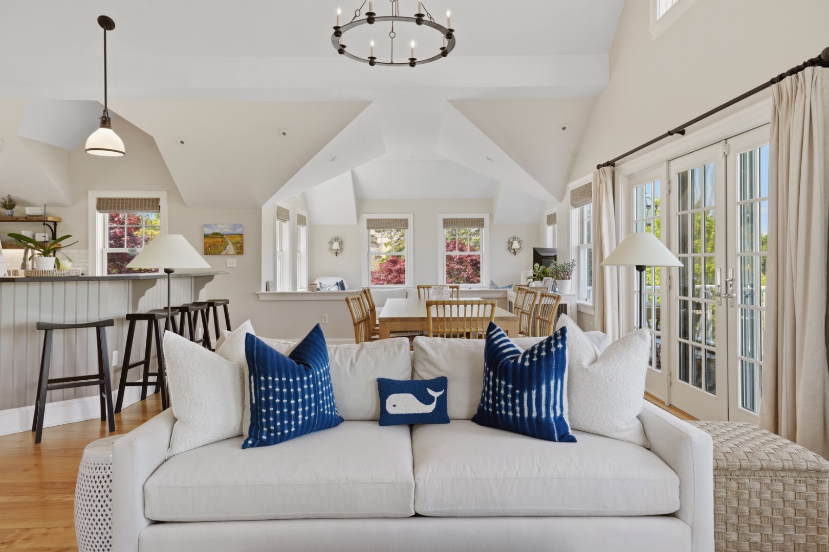 Open-plan living and dining room with vaulted ceiling, white sofa, navy pillows, and glass doors.