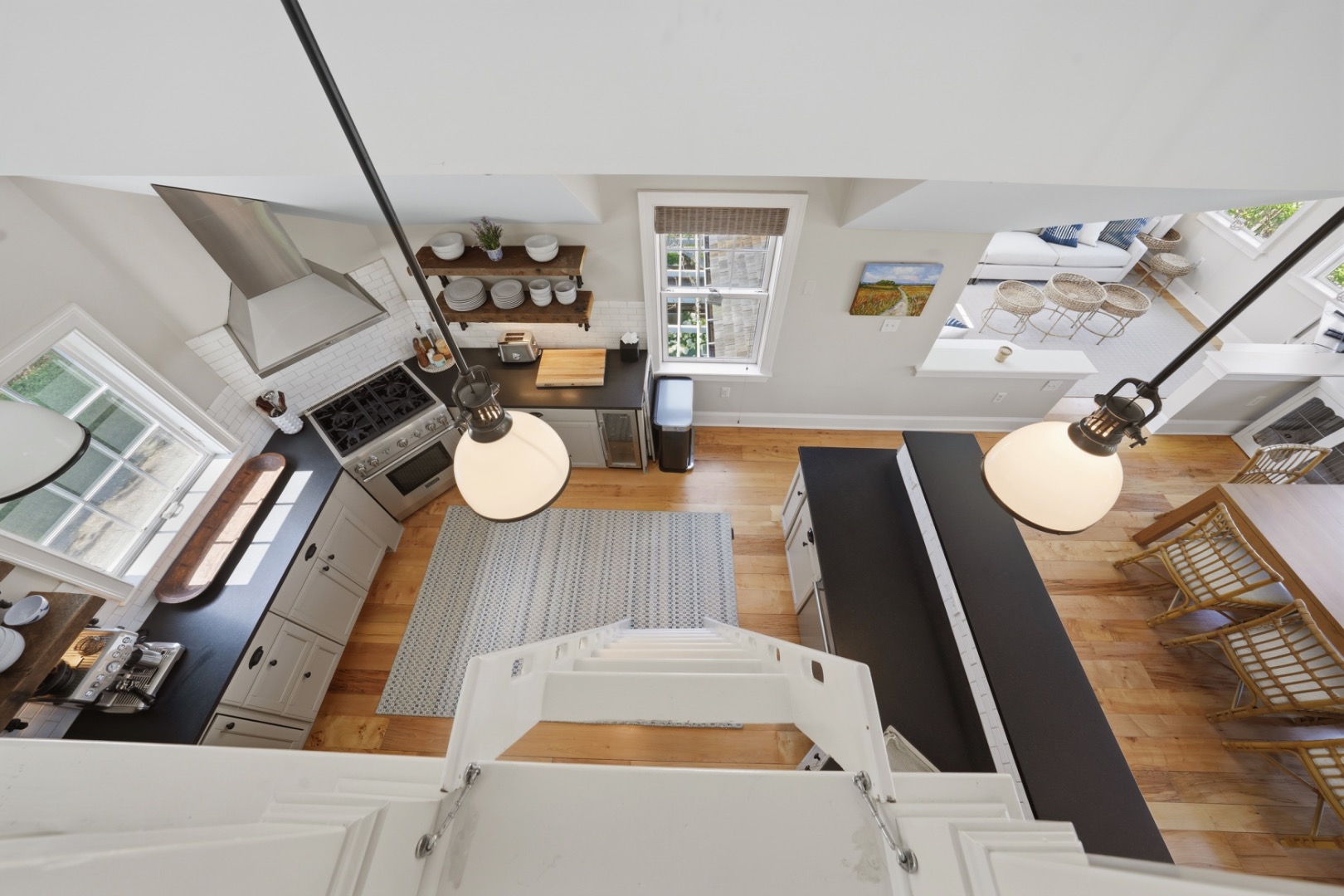 Kitchen viewed from above, with black countertops, open dish shelves, and a stairway in the foreground.
