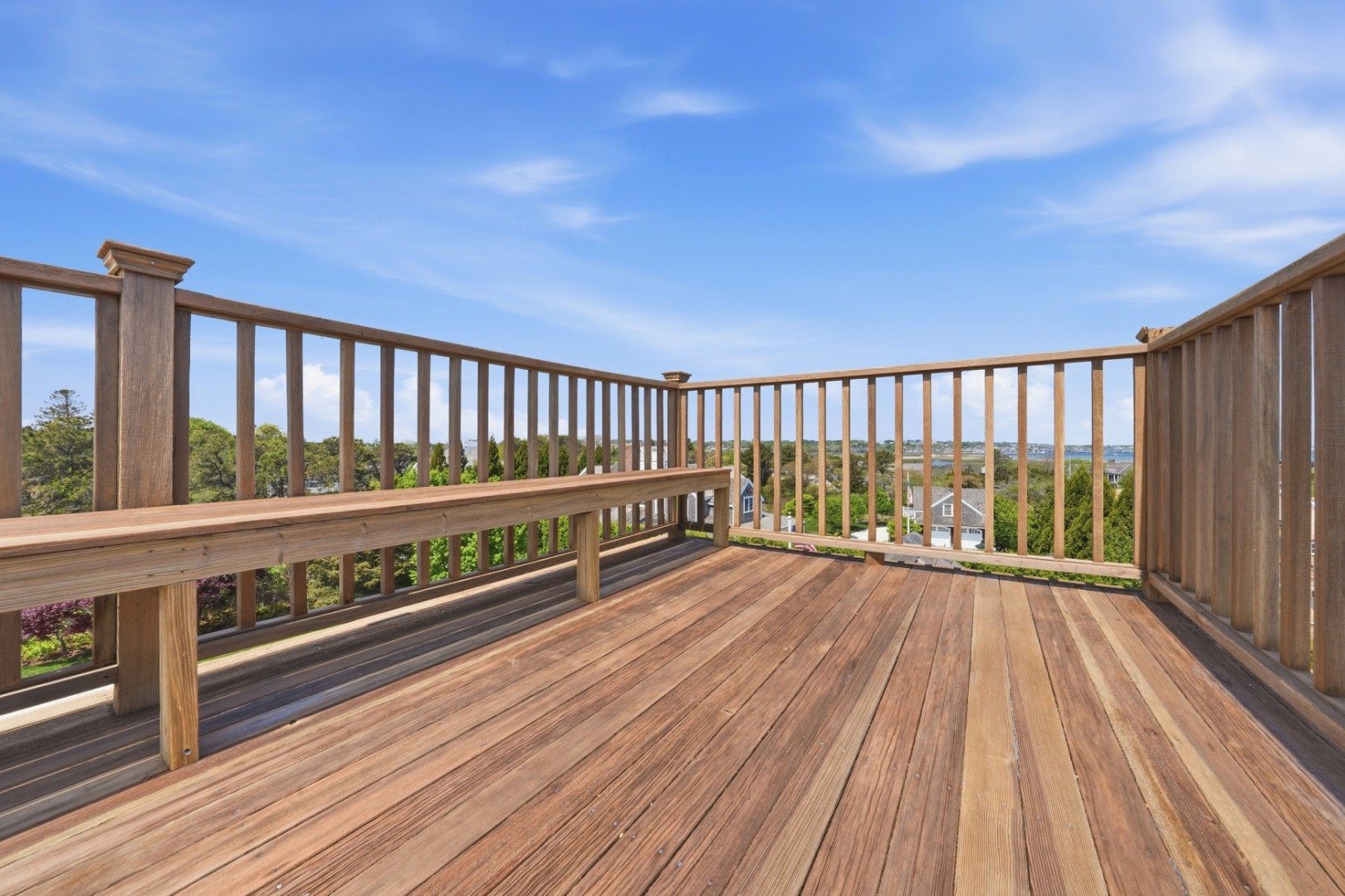 Wooden rooftop deck with built-in bench seating overlooking homes and distant water.