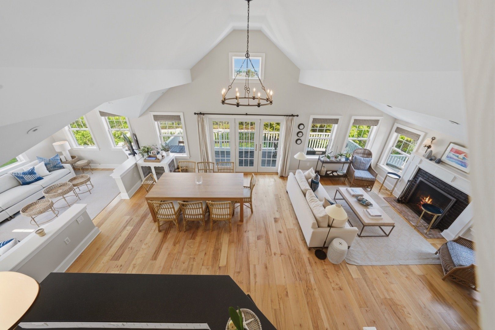 Vaulted living and dining room with French doors to a deck, pale wood floors, and a fireplace.