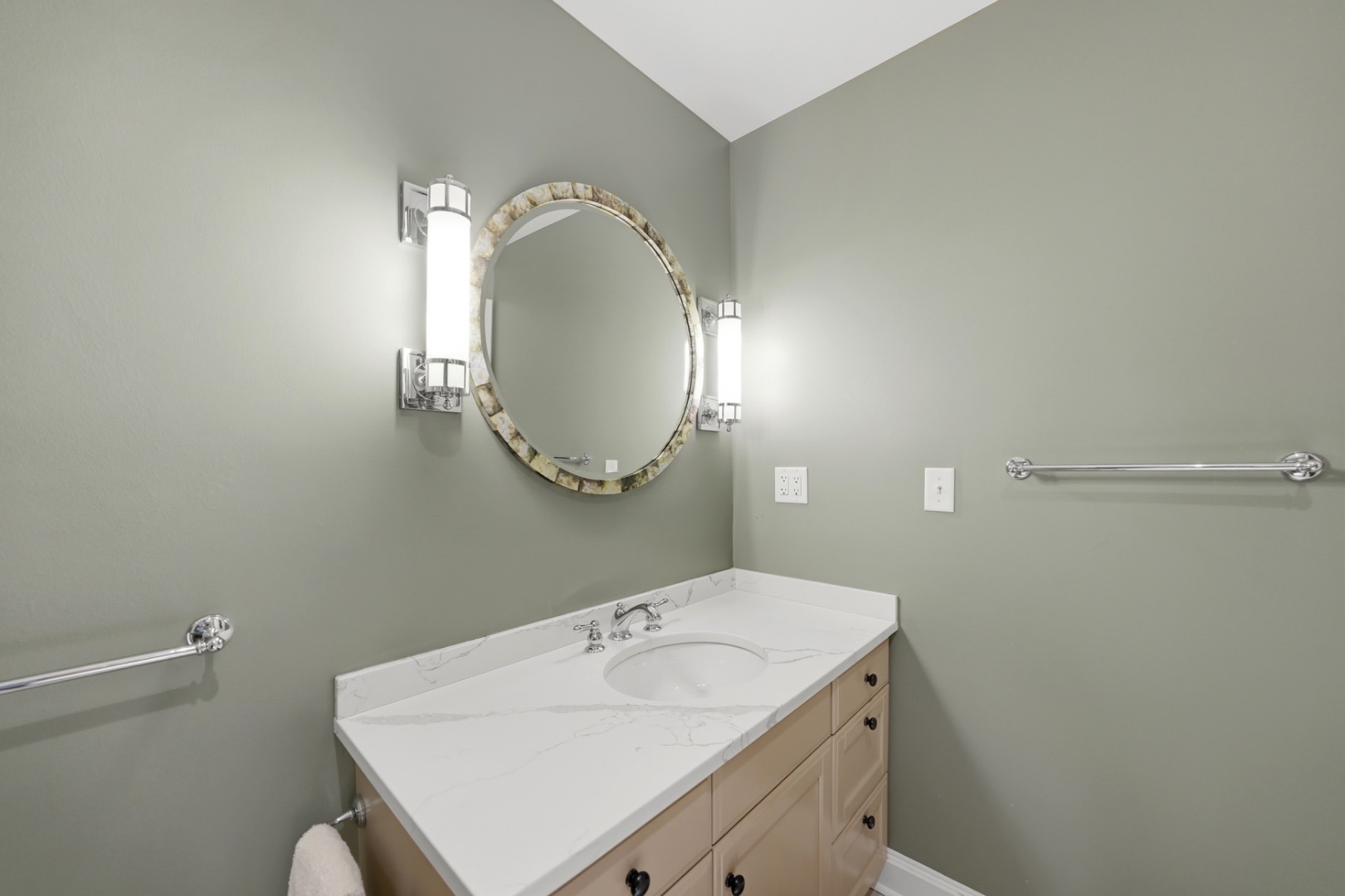 Bathroom vanity with a veined white countertop, round mirror, and chrome grab bars.