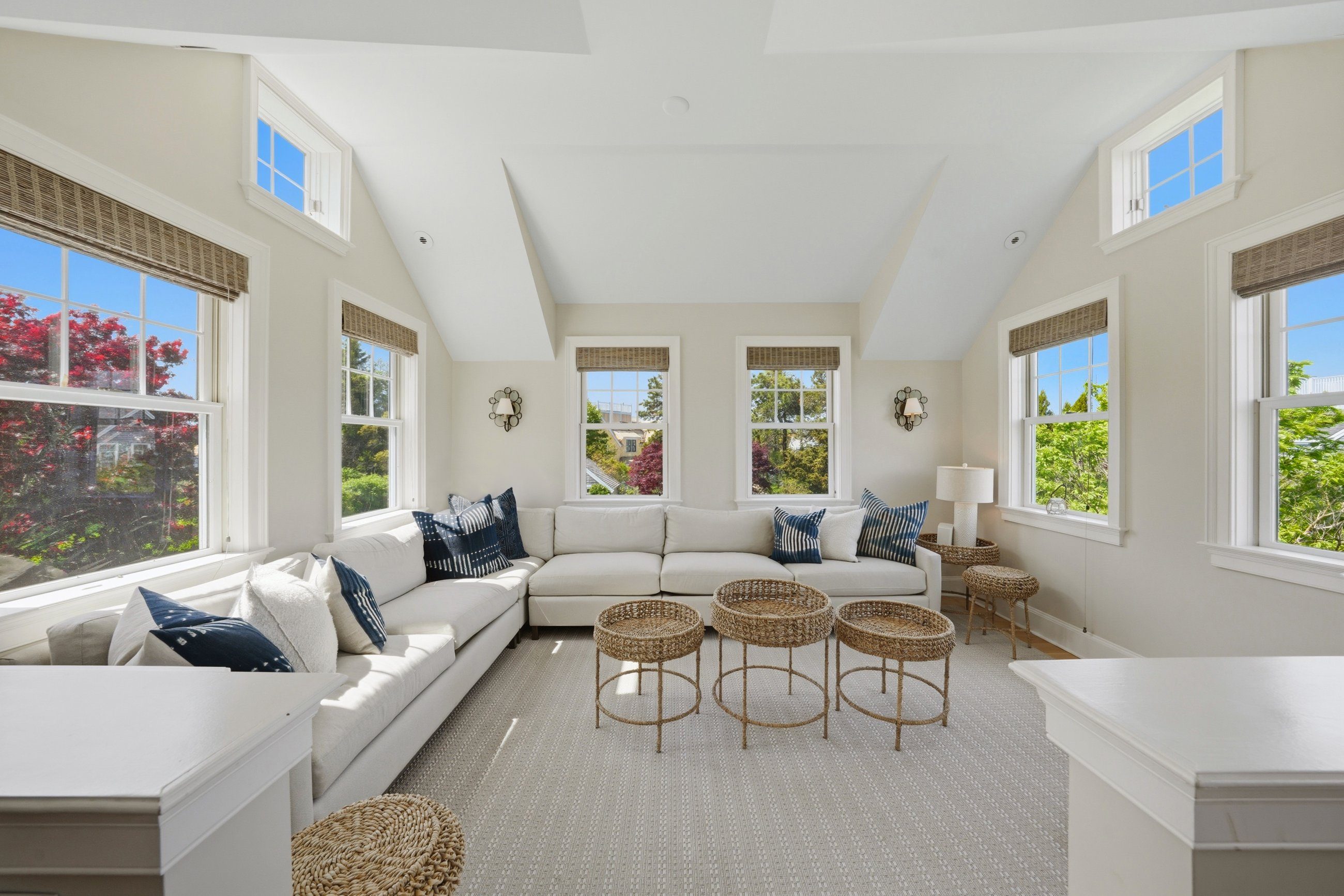 Living room with a vaulted ceiling, white sectional sofa, woven stools, and large windows.