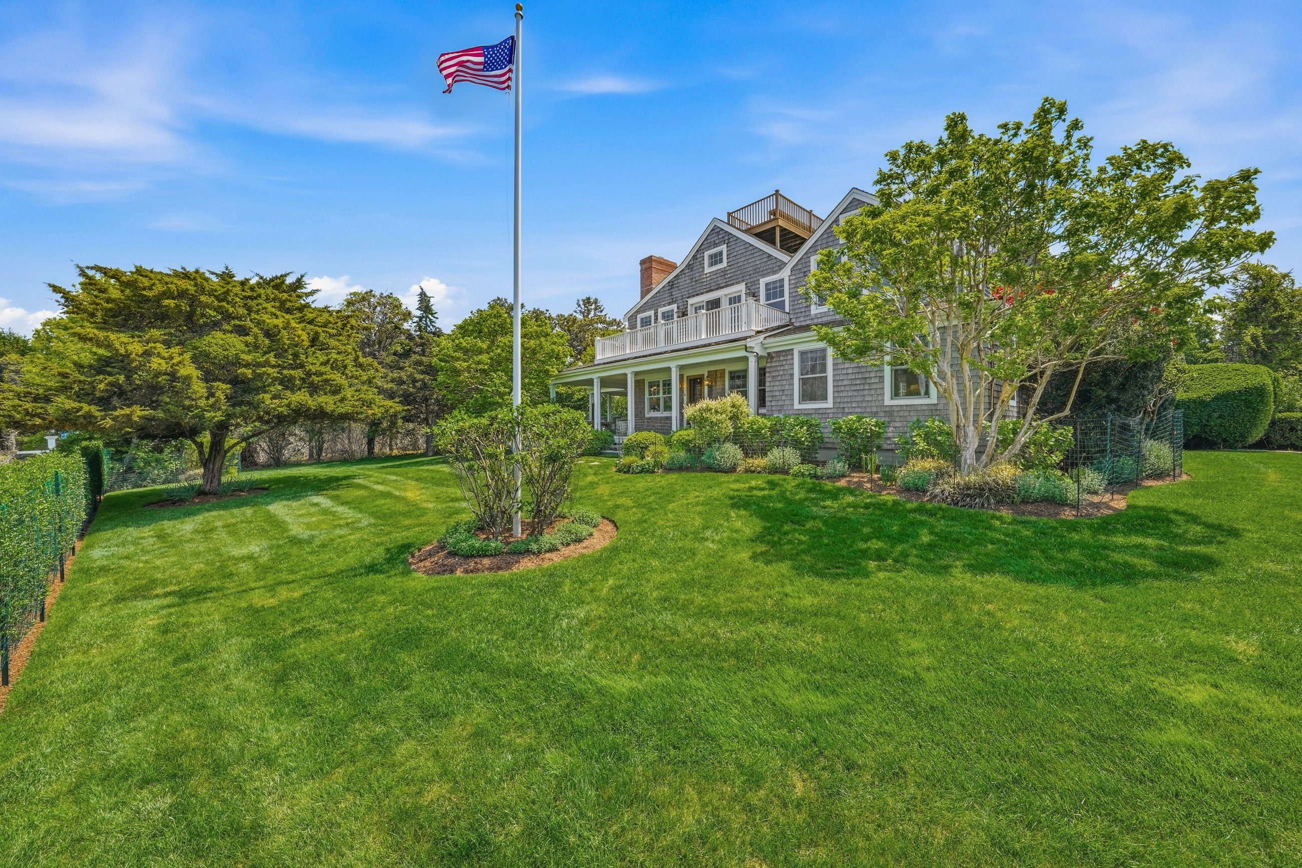 Gray shingle house with upper decks behind a broad lawn and an American flag.