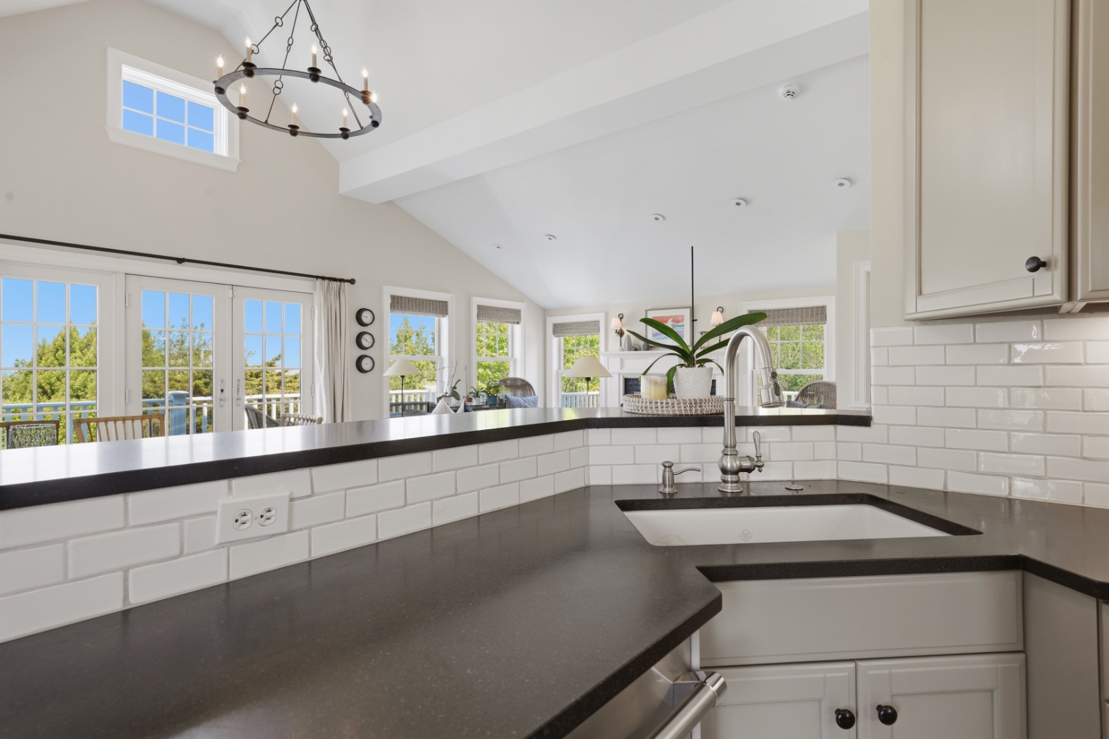 Bright kitchen with dark countertops, a farmhouse sink, white tile backsplash, and French doors.