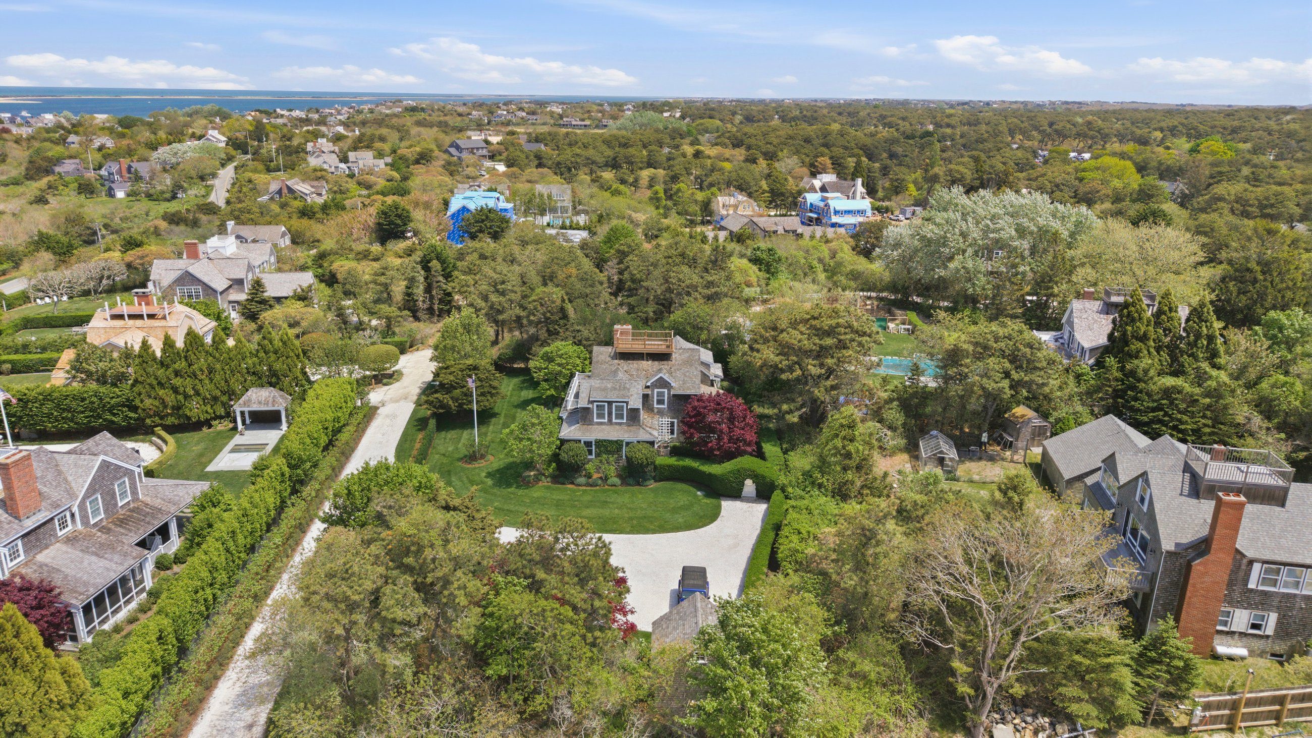 Aerial view of a shingle-style home and landscaped grounds, with the ocean in the distance.