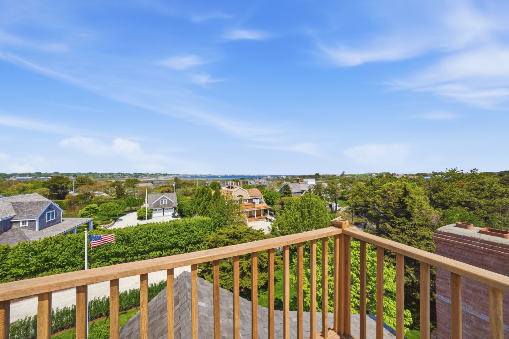 Wooden rooftop deck overlooking leafy homes and distant water on Nantucket.