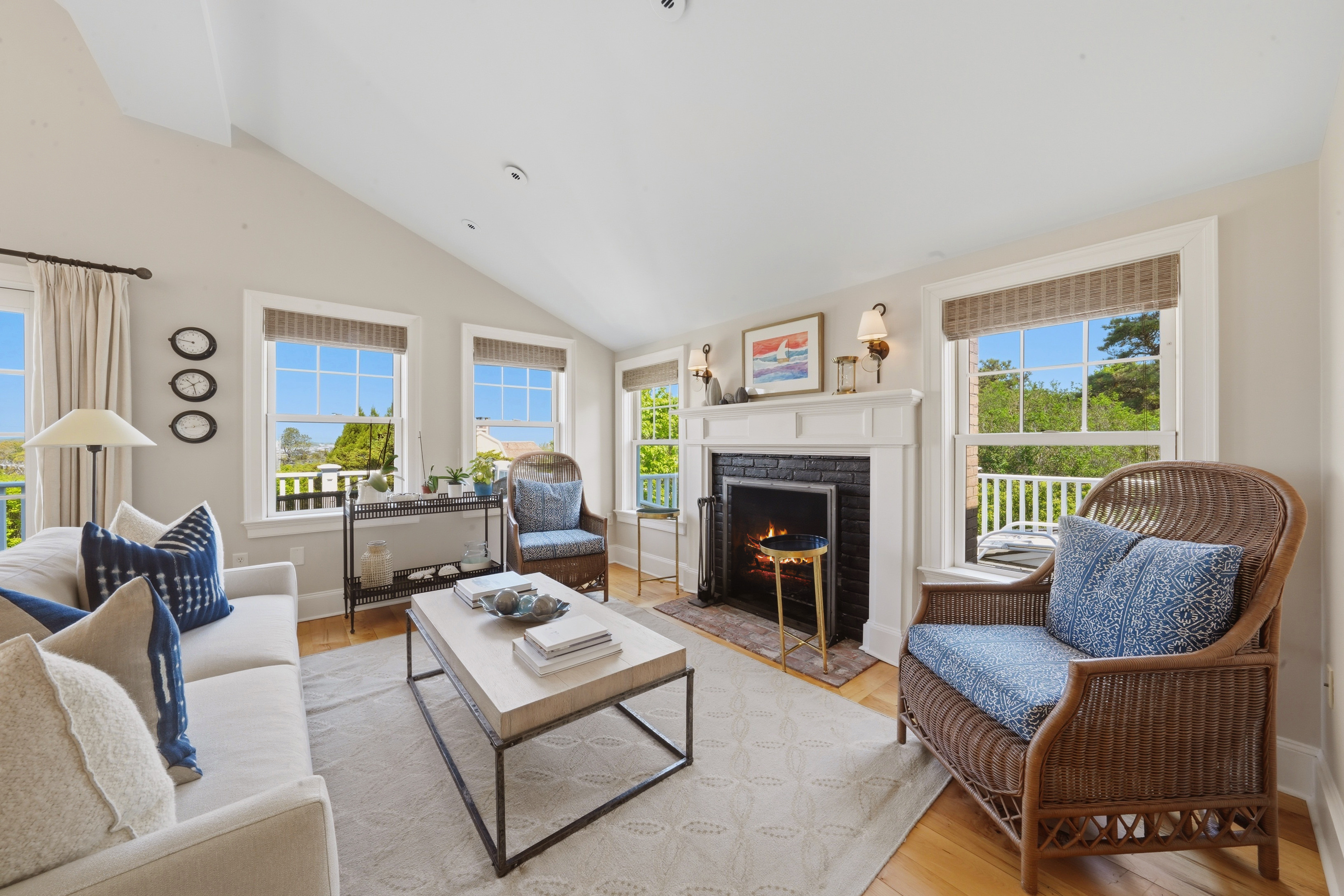 Living room with a vaulted ceiling, white fireplace, wicker chairs, and windows with a water view.