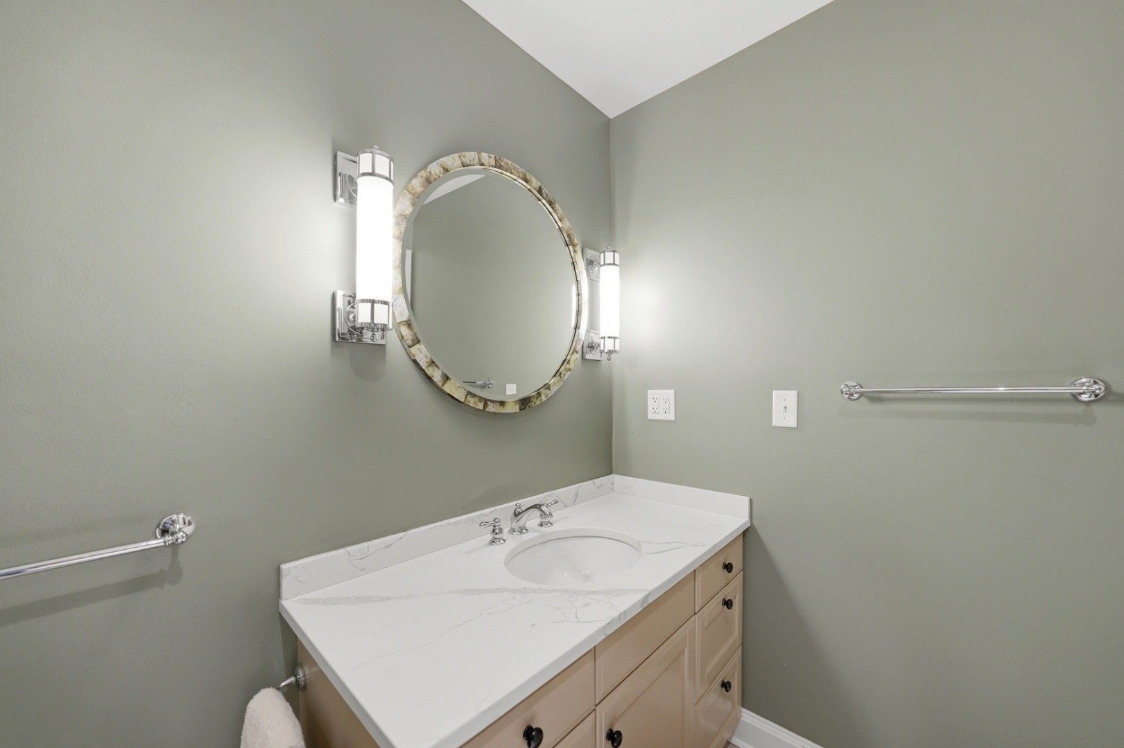 Bathroom vanity with a veined white countertop, oval mirror, and grab bars.