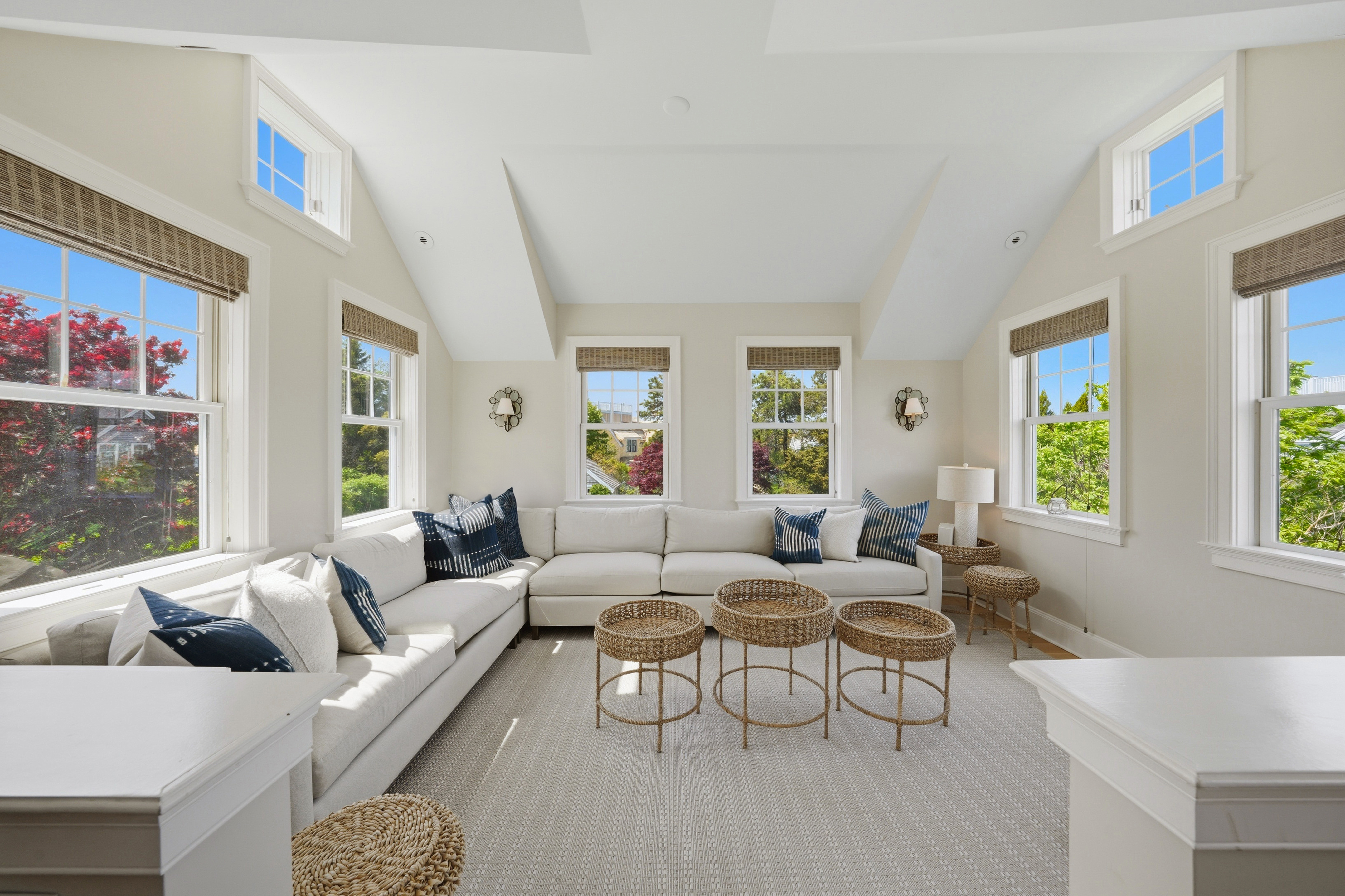 Bright sitting room with a white sectional, woven coffee tables, and large windows.