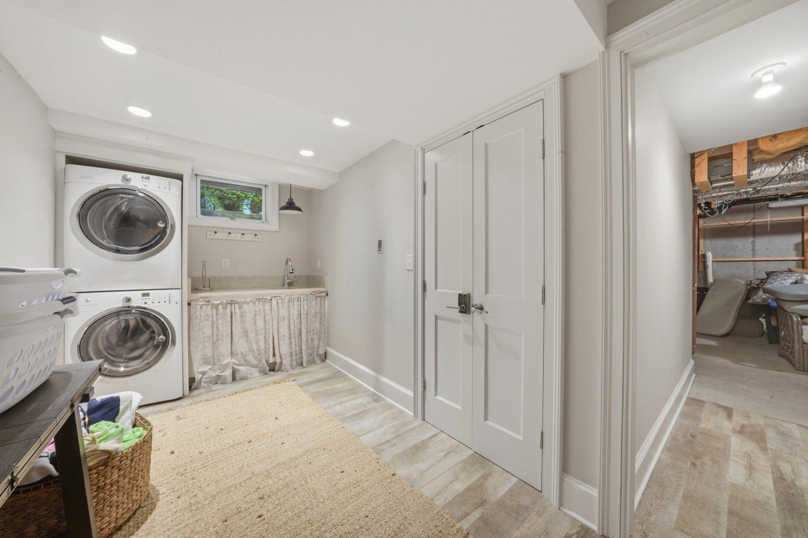Laundry room with stacked washer and dryer, skirted utility sink, and doorway to an unfinished area.