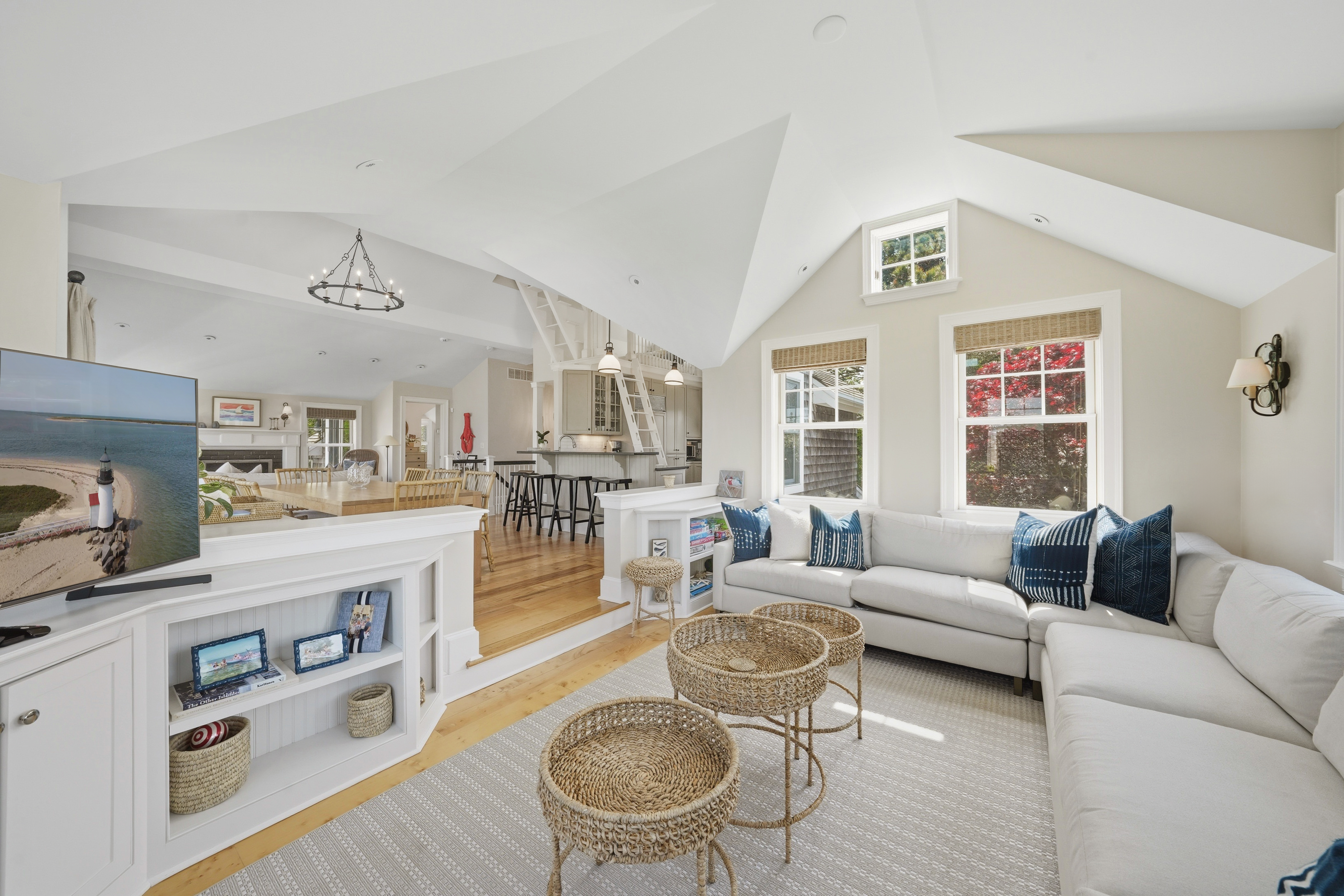 Open-plan living room with a vaulted ceiling, white sectional, woven coffee tables, and connected kitchen and dining area.